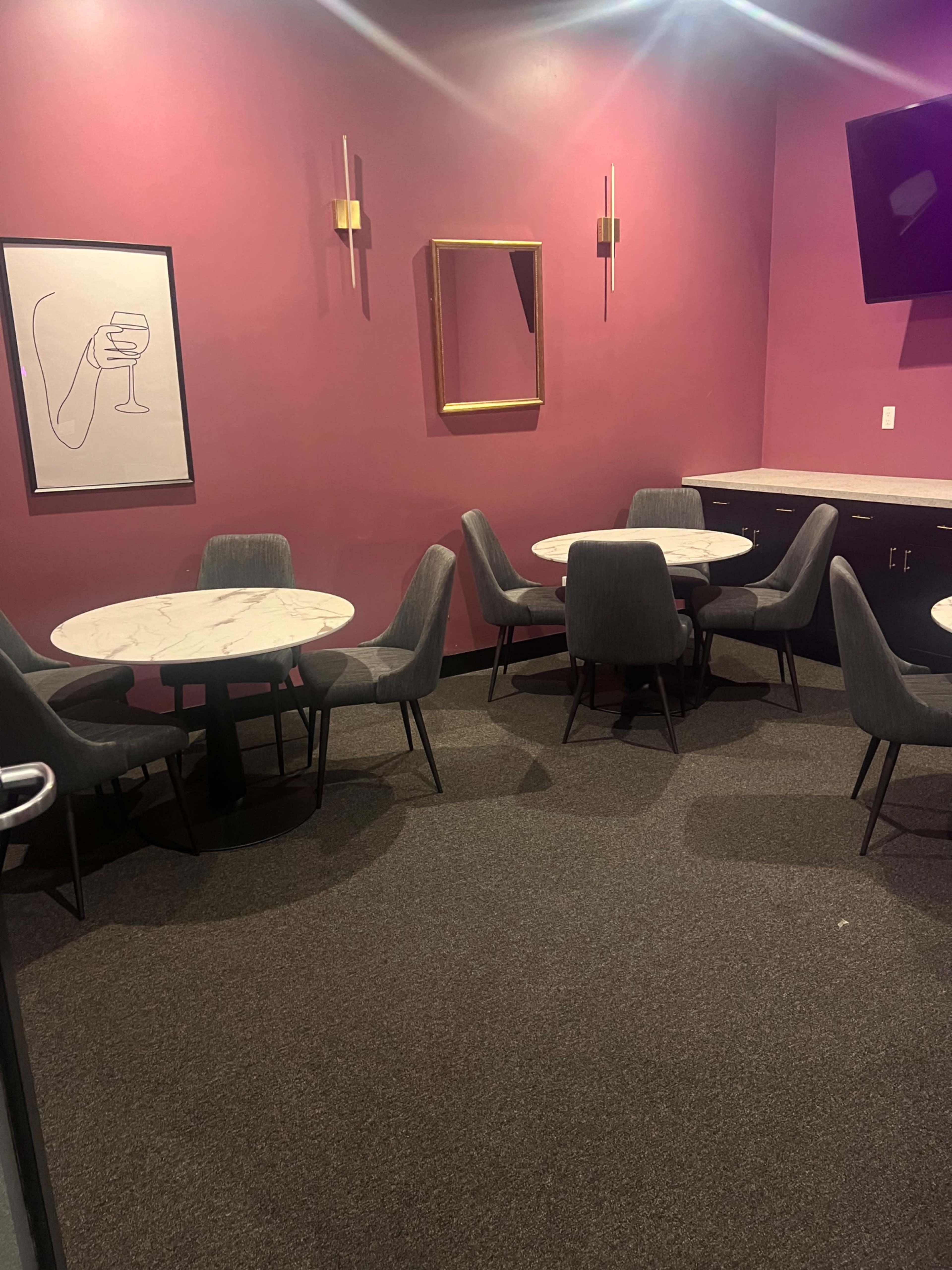 A small dining area with marble-top tables and gray upholstered chairs against a pink wall.