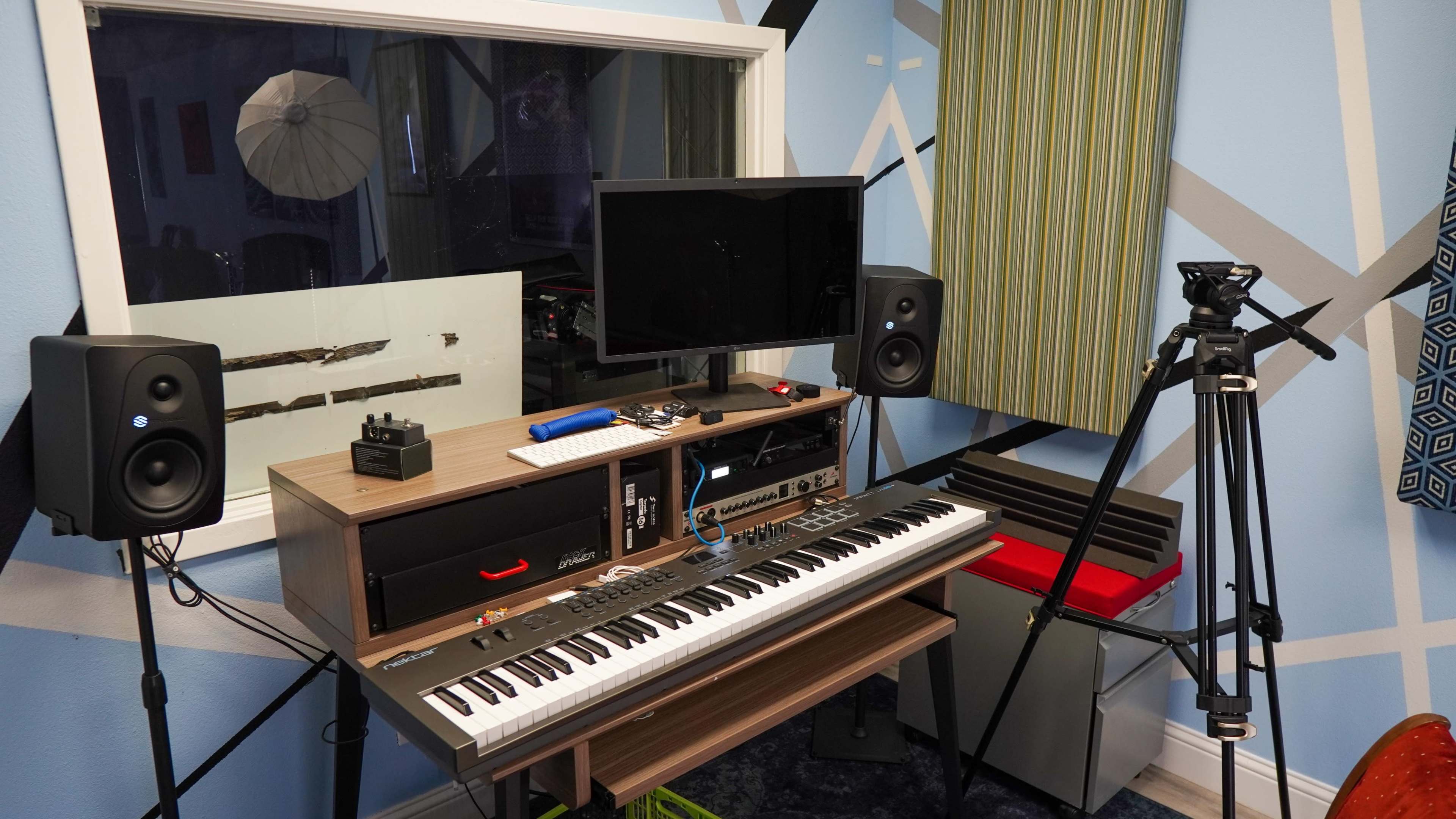A music production setup featuring a keyboard, a monitor, and audio speakers in a colorful room.