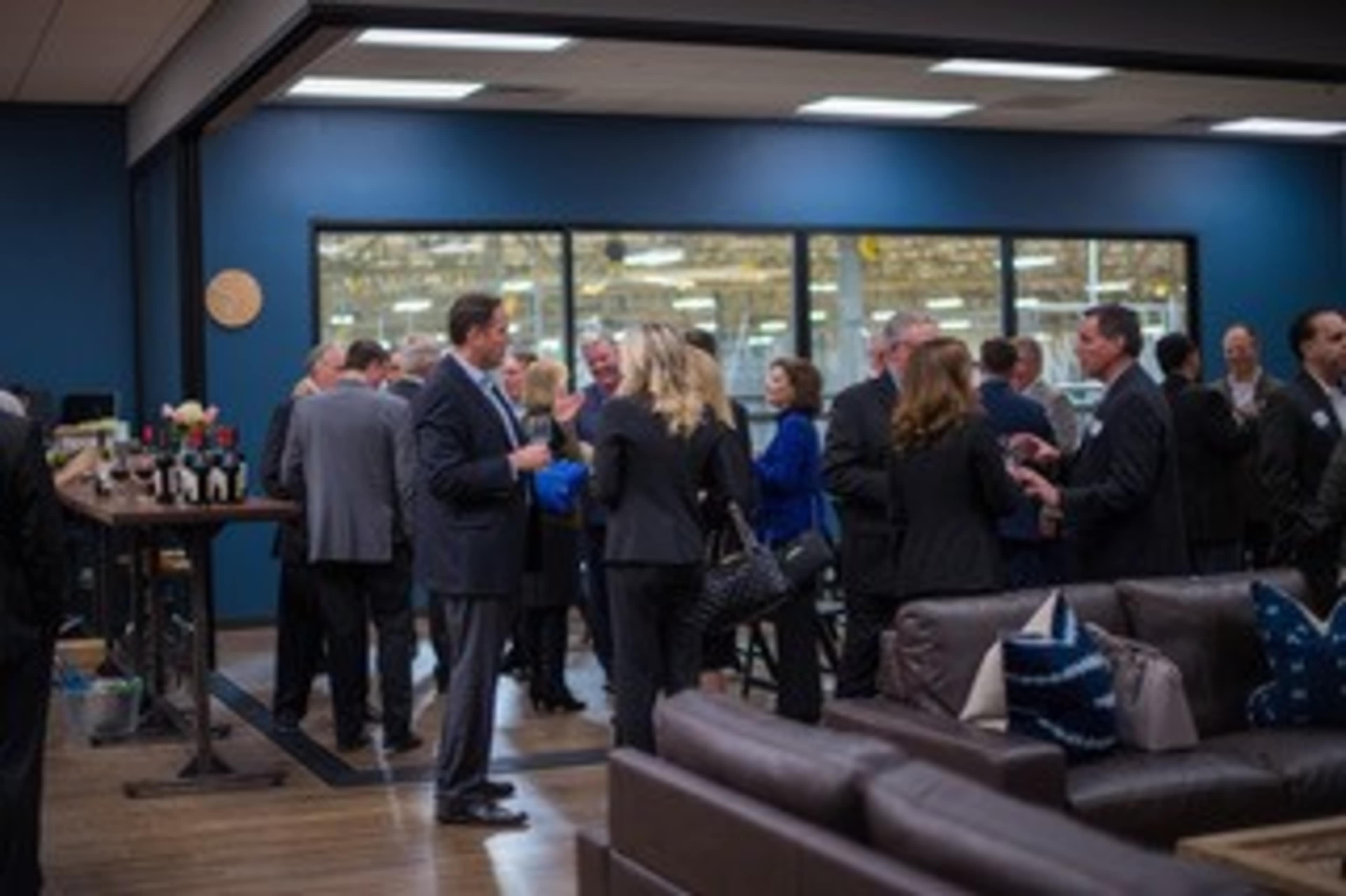 A group of people in business attire engage in conversation at a networking event in a well-lit office space.