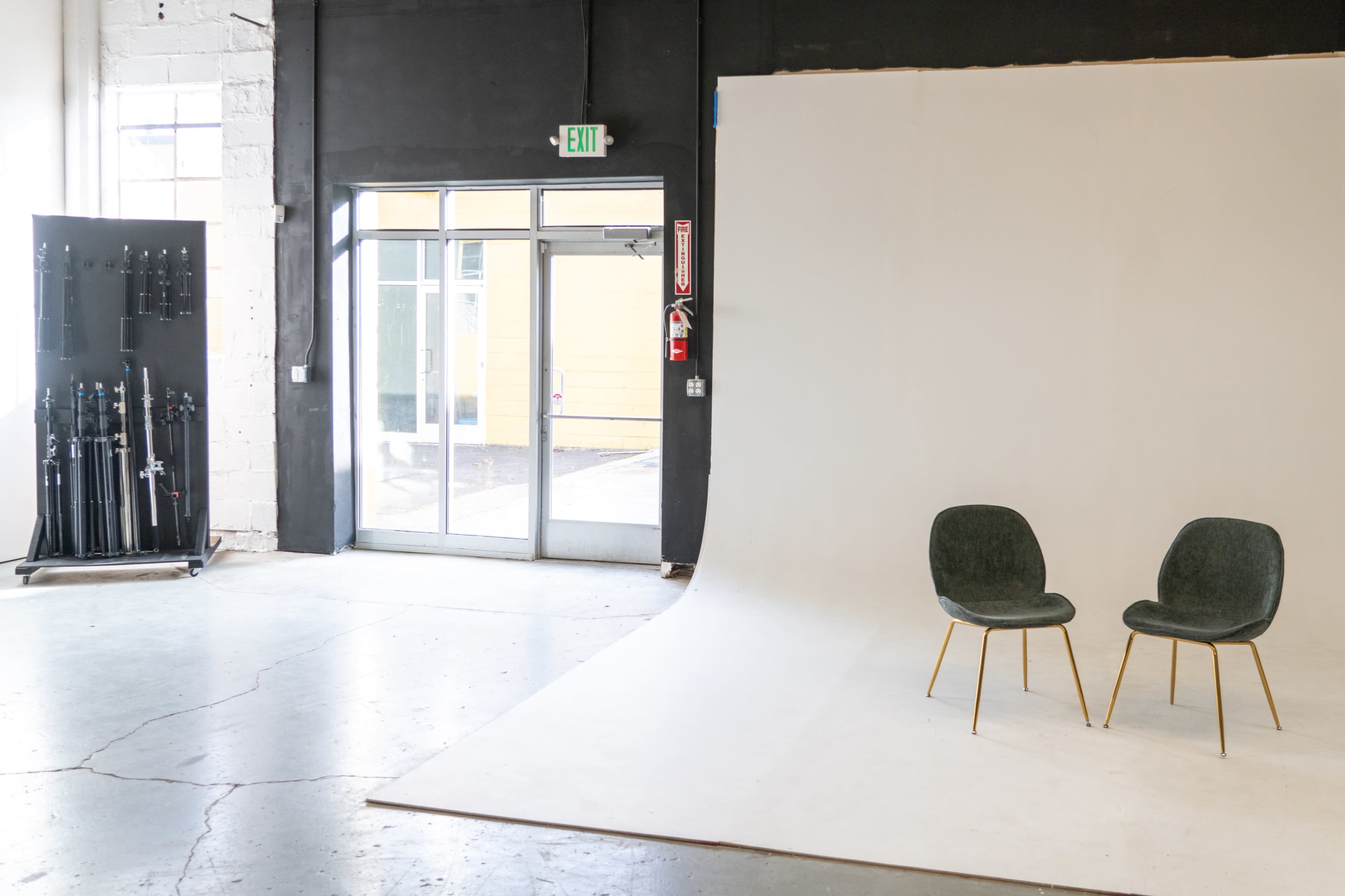 The image shows a minimalistic photography studio with a light-colored backdrop and two green chairs facing each other.