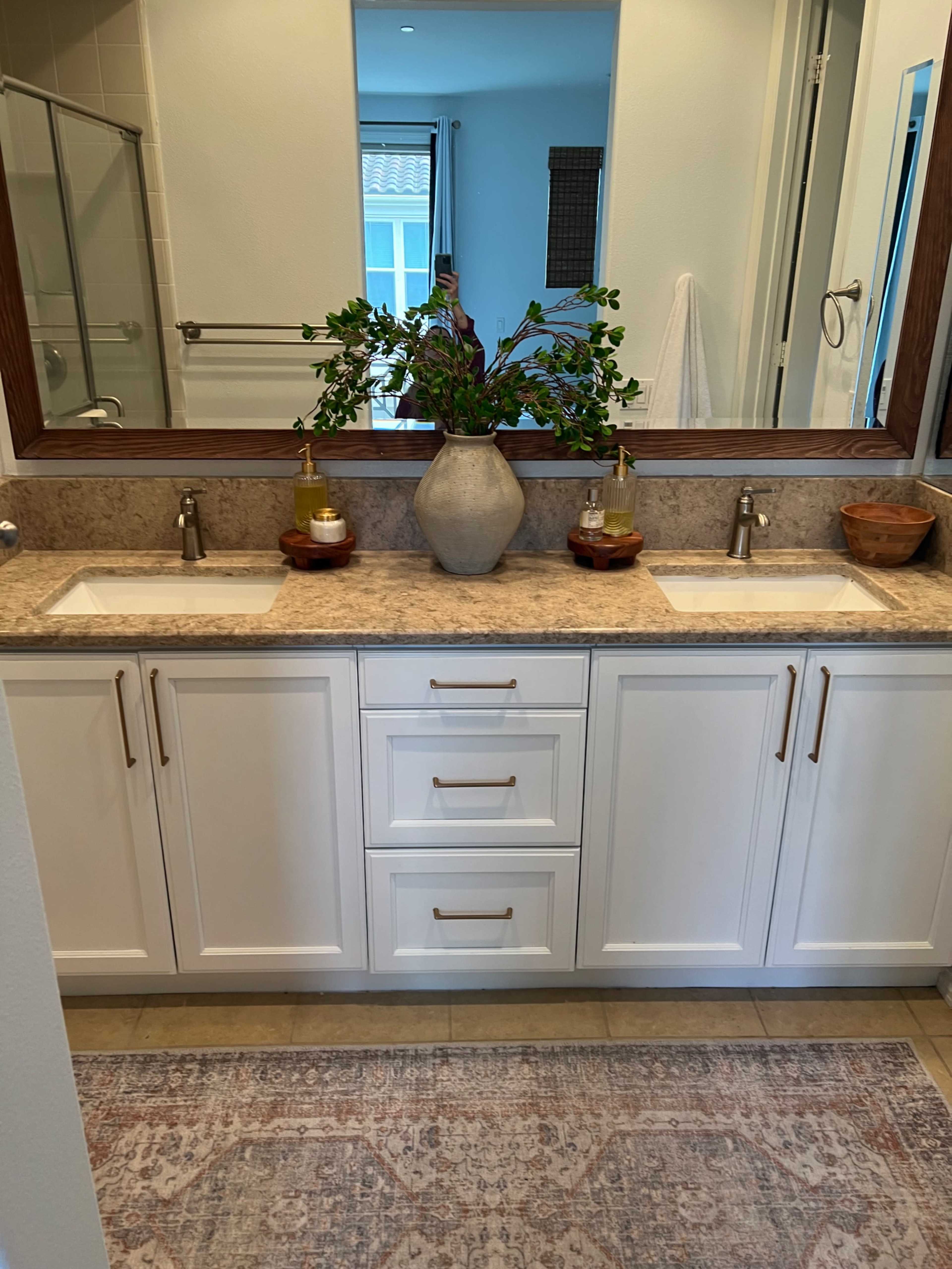 A modern bathroom features a double sink vanity with a stone countertop, decorative plants, and neutral-colored decor.