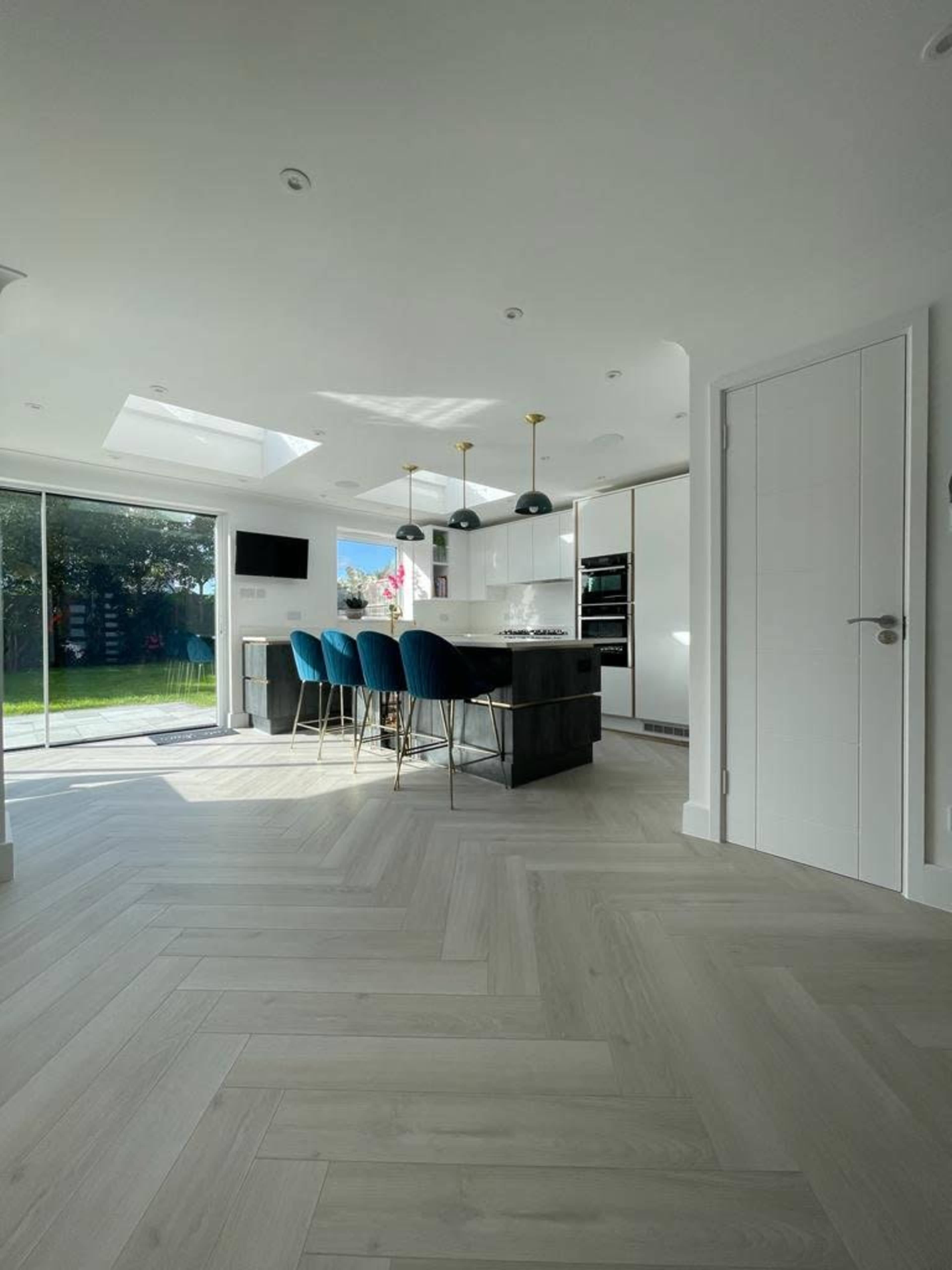 A modern kitchen features a central island with bar stools, large windows allowing natural light, and sleek cabinetry.
