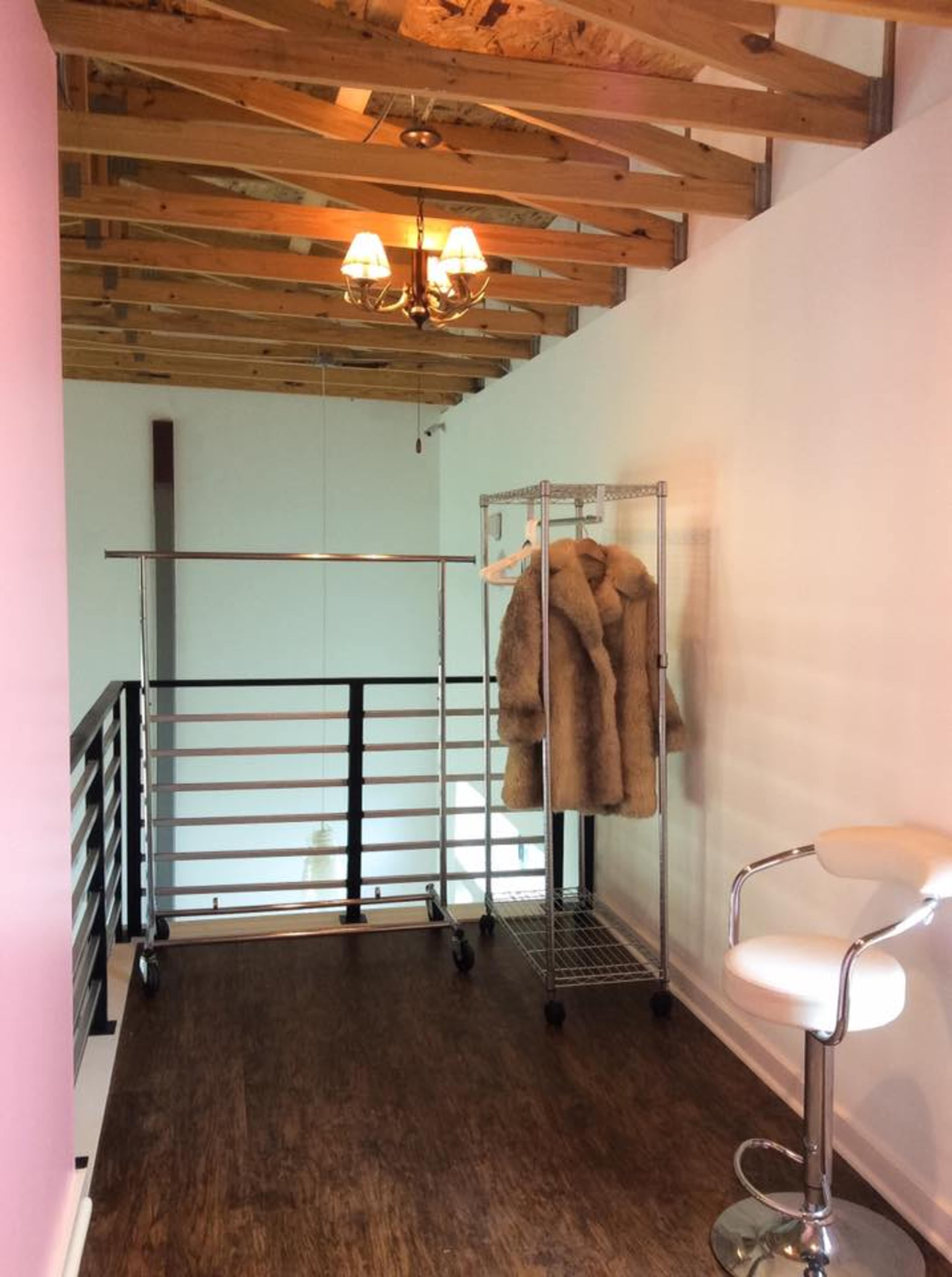 A spacious loft area features a clothing rack with fur coats, a bar stool, and exposed wooden beams overhead.