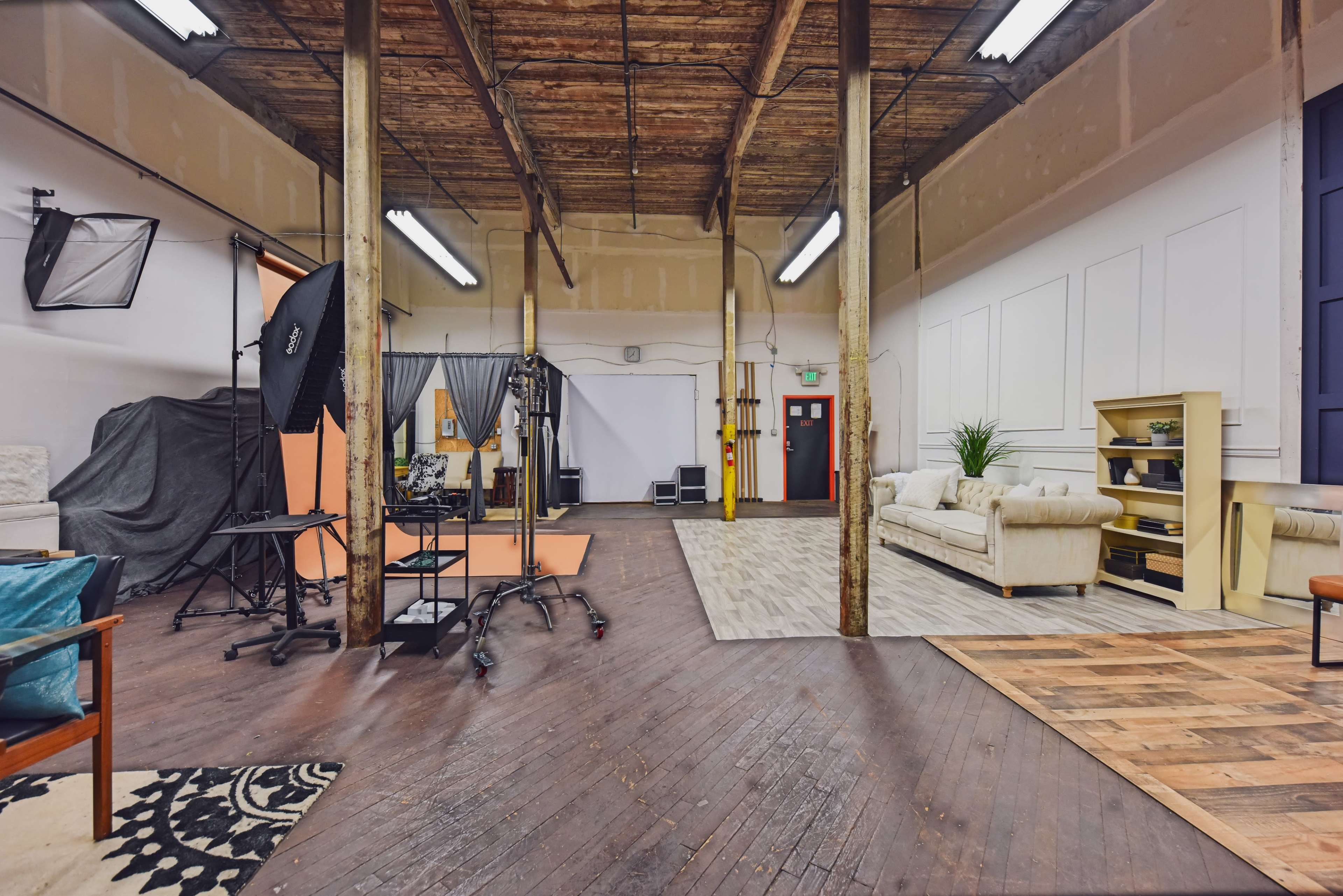 The image shows a spacious studio with wooden floors, large pillars, photography equipment, and a furnished lounge area.