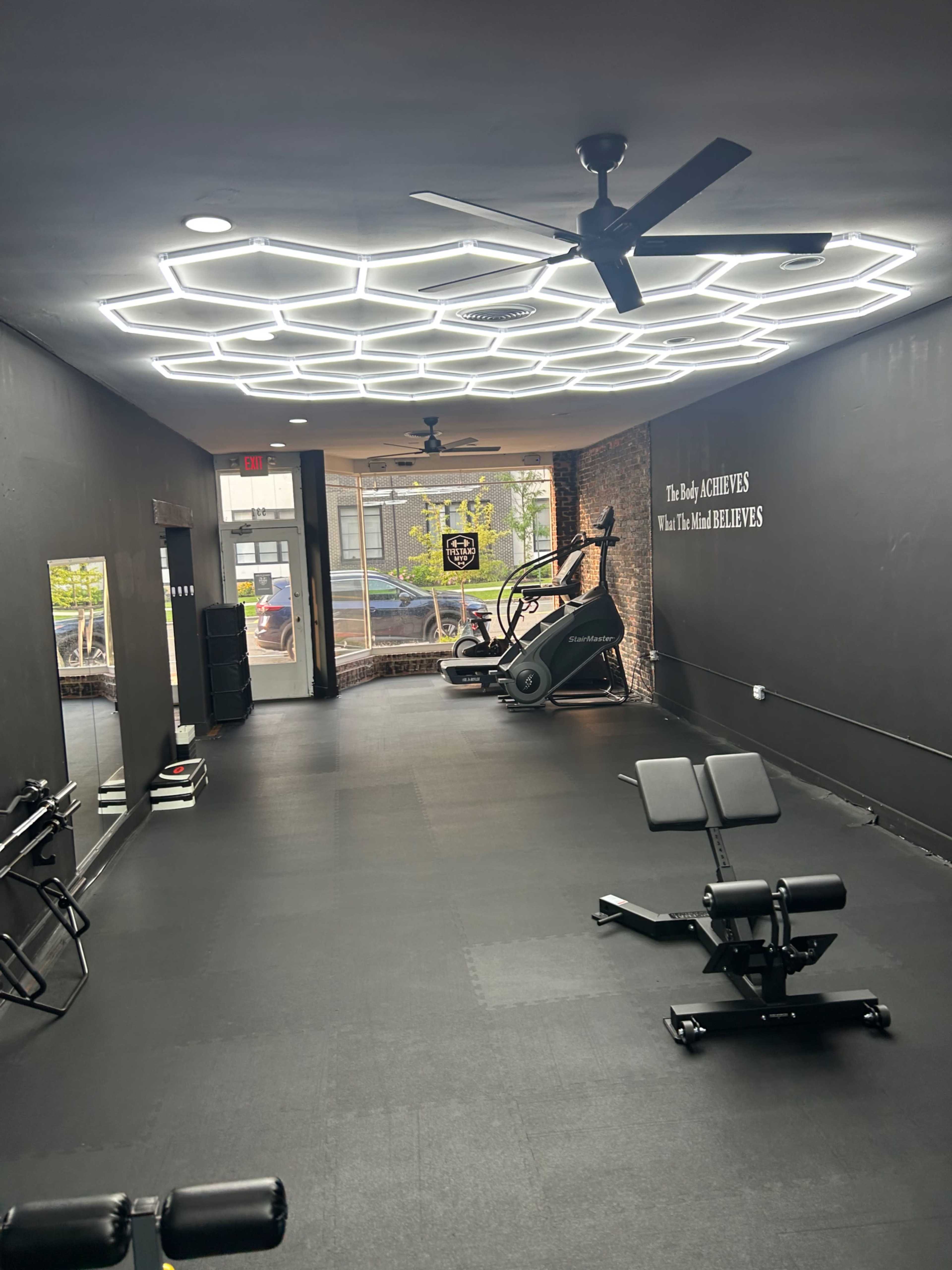 The image shows a modern gym with black walls, hexagonal LED lighting, a mirrored wall, and various workout equipment.