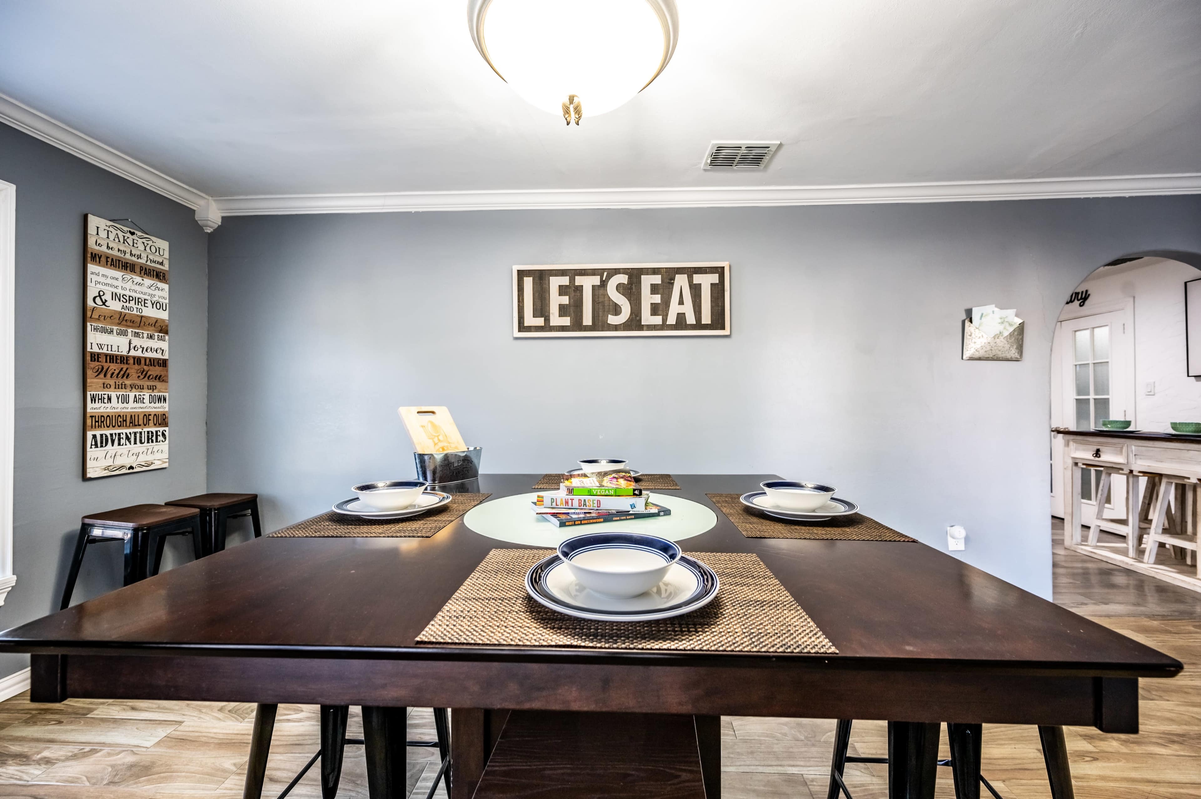 A dining table is set with plates and utensils in a room featuring a wall sign that says "LET'S EAT."