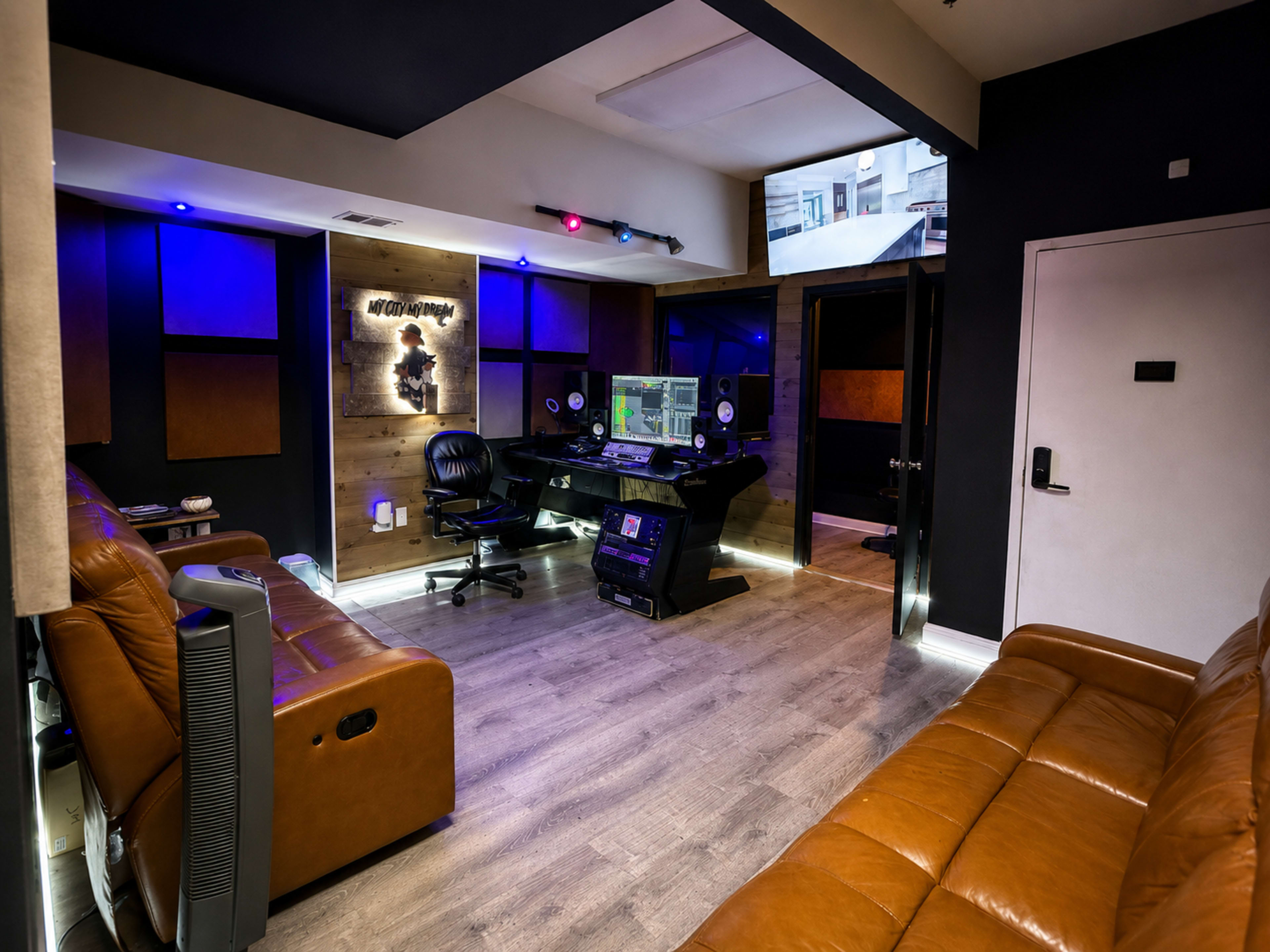 The image shows a modern recording studio featuring a central mixing console, soundproofed walls, and leather couches.
