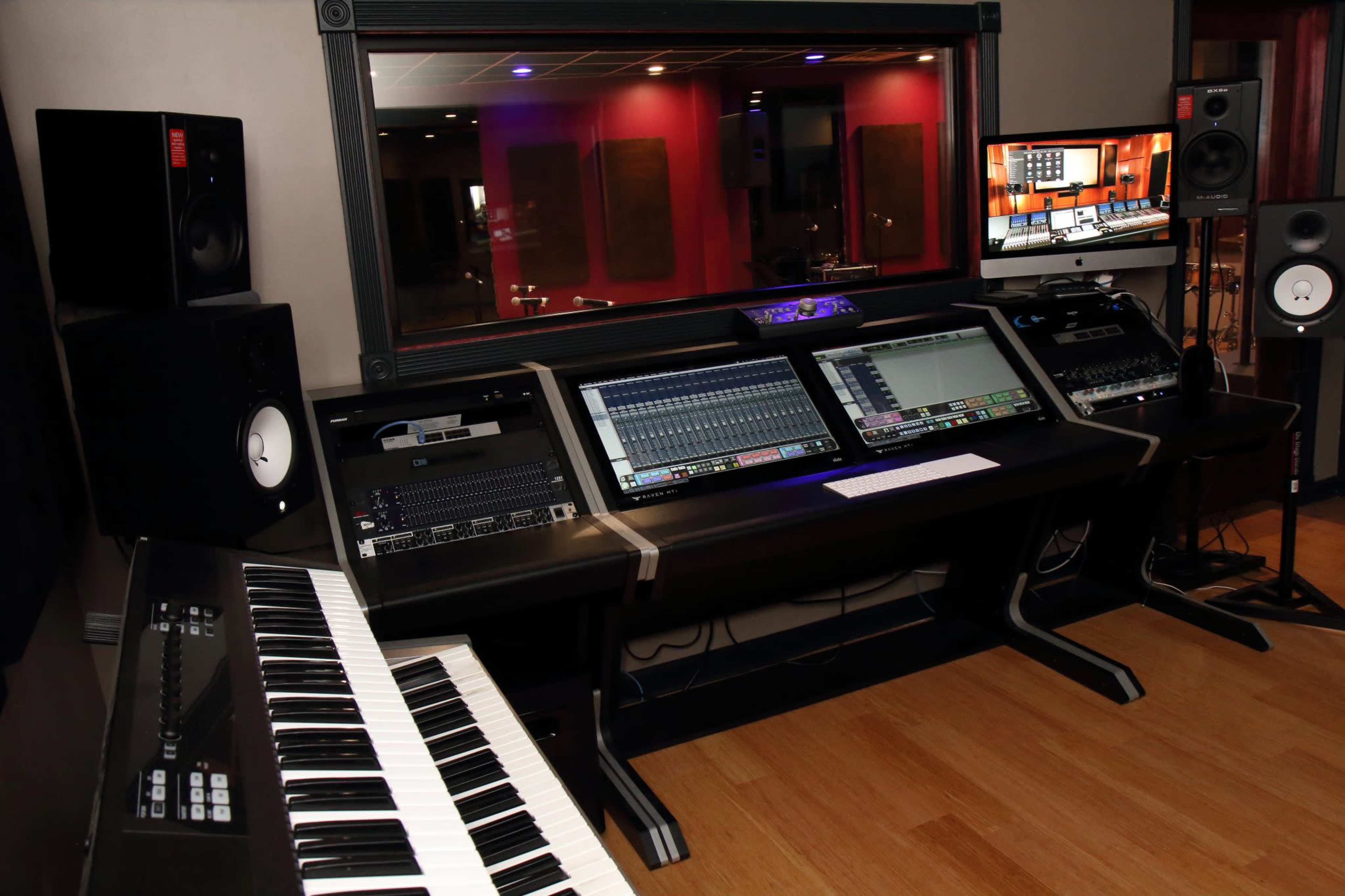 A modern music studio with a keyboard, multiple sound mixing consoles, and monitors arranged on a sleek desk.