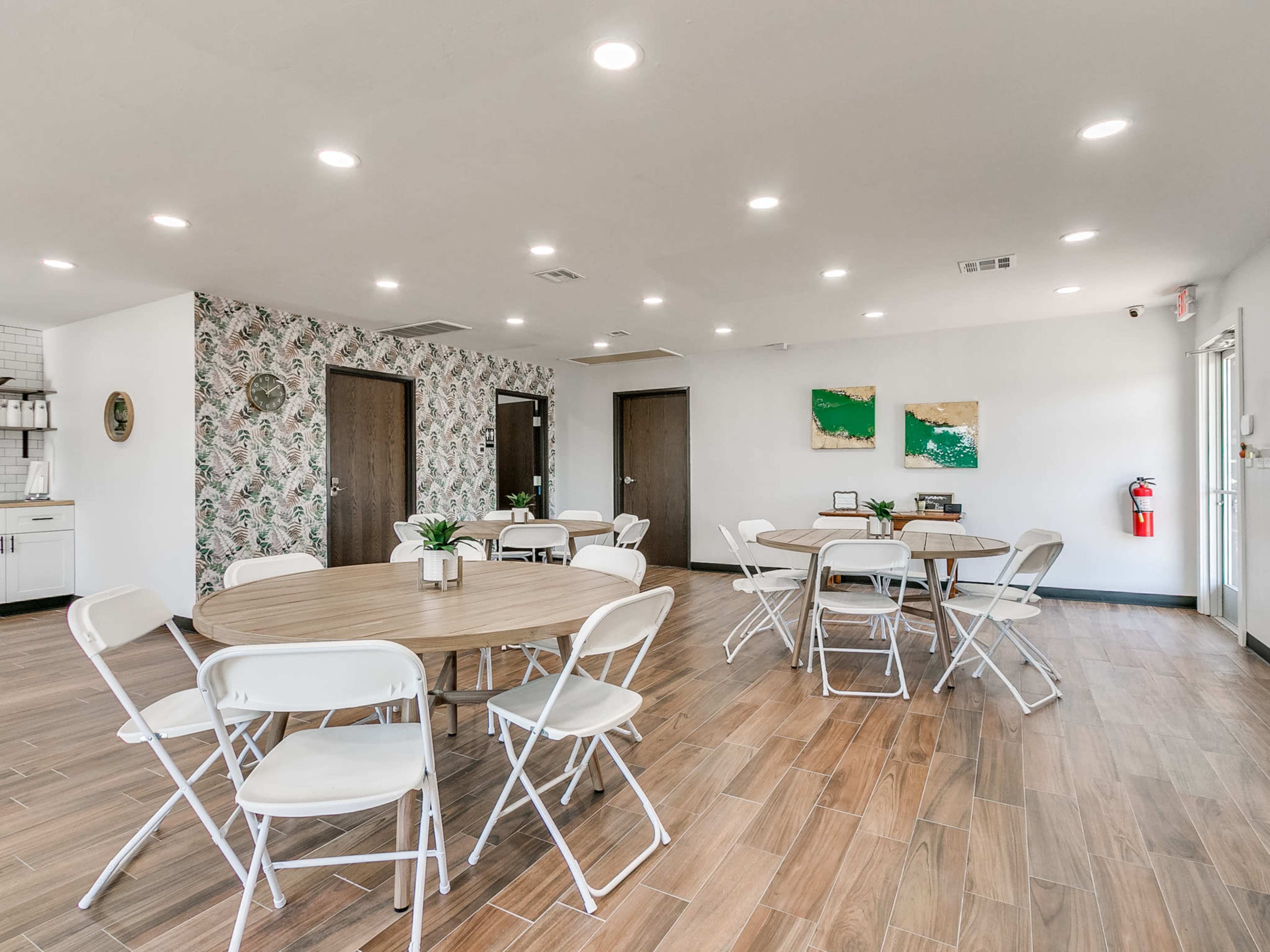 A spacious, well-lit room with several round tables and white chairs arranged around them.