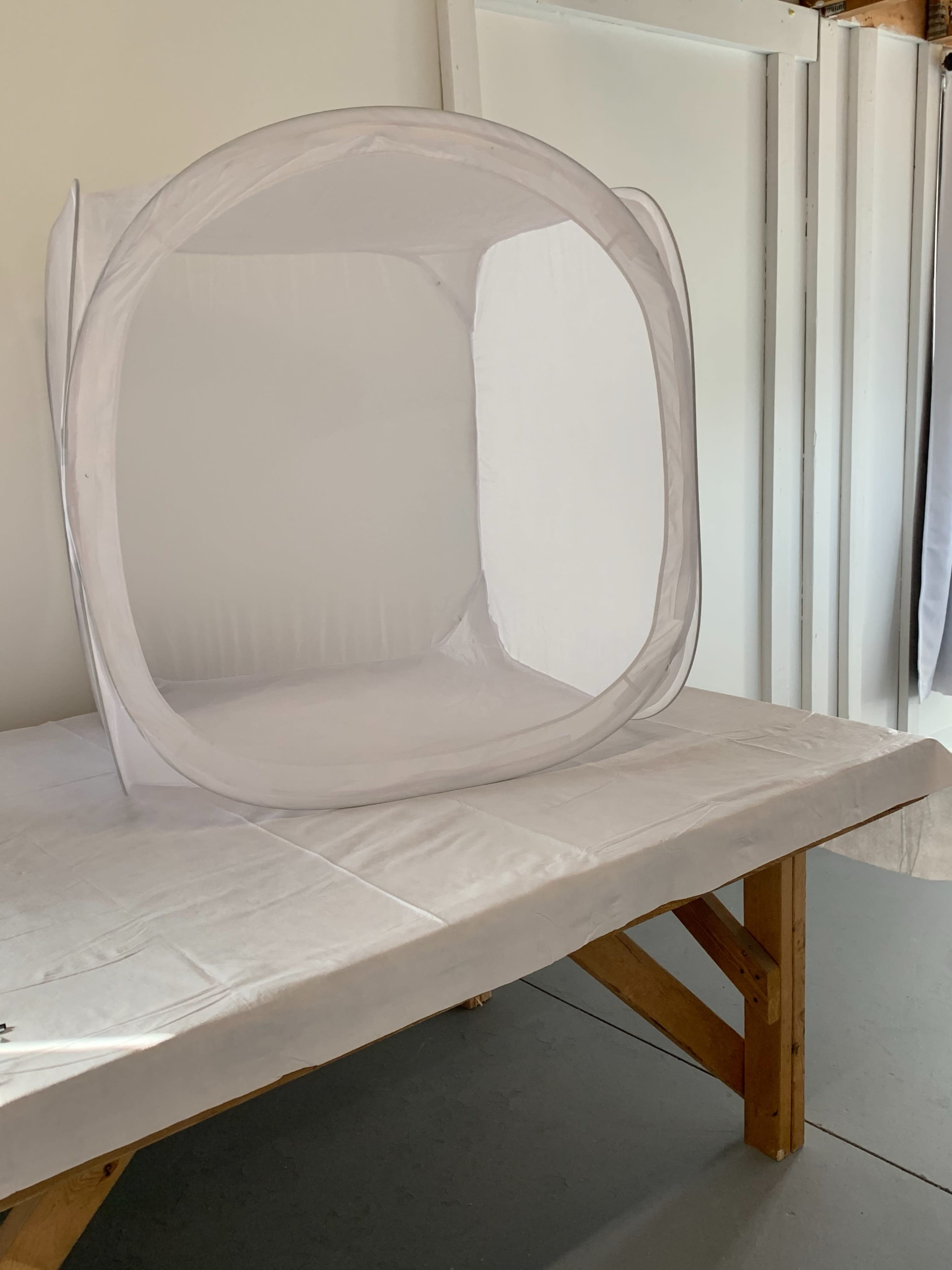 A transparent white photo booth is set up on a wooden table in a plain room.