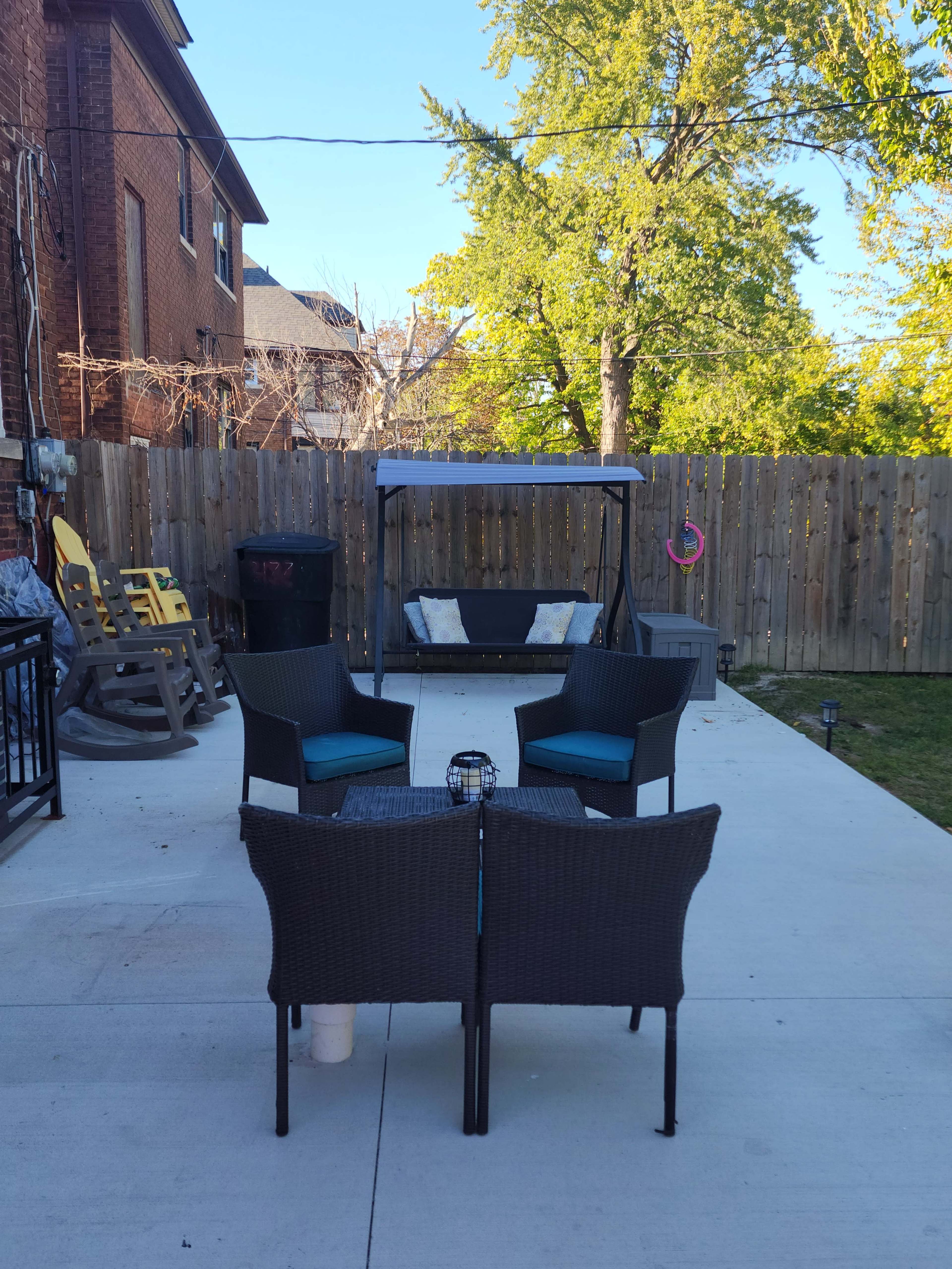 A backyard patio with four chairs arranged around a small table, a swing hang, and a wooden fence in the background.