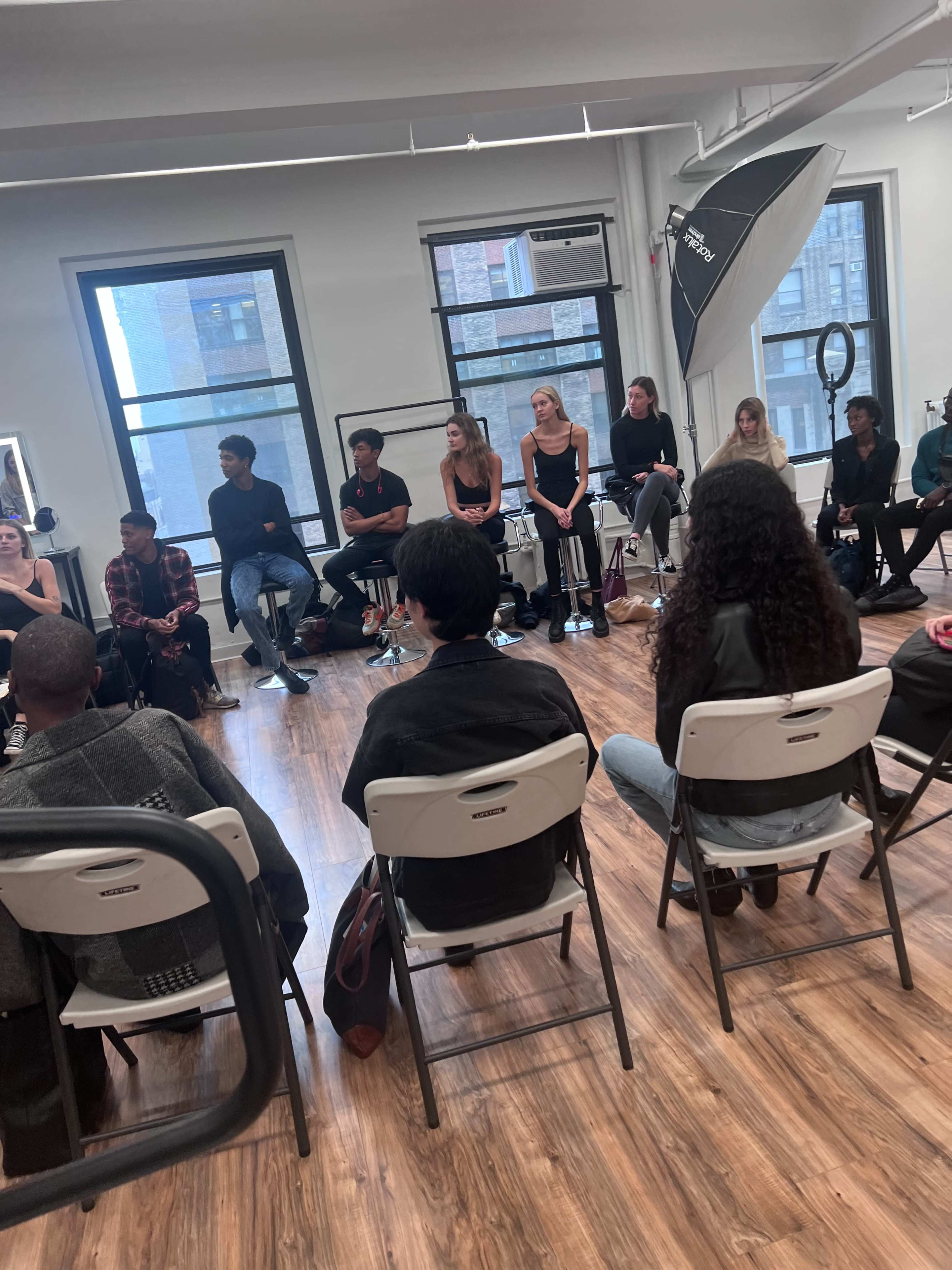 A group of people are seated in a brightly lit room, facing an audience of individuals in chairs arranged in a circle.