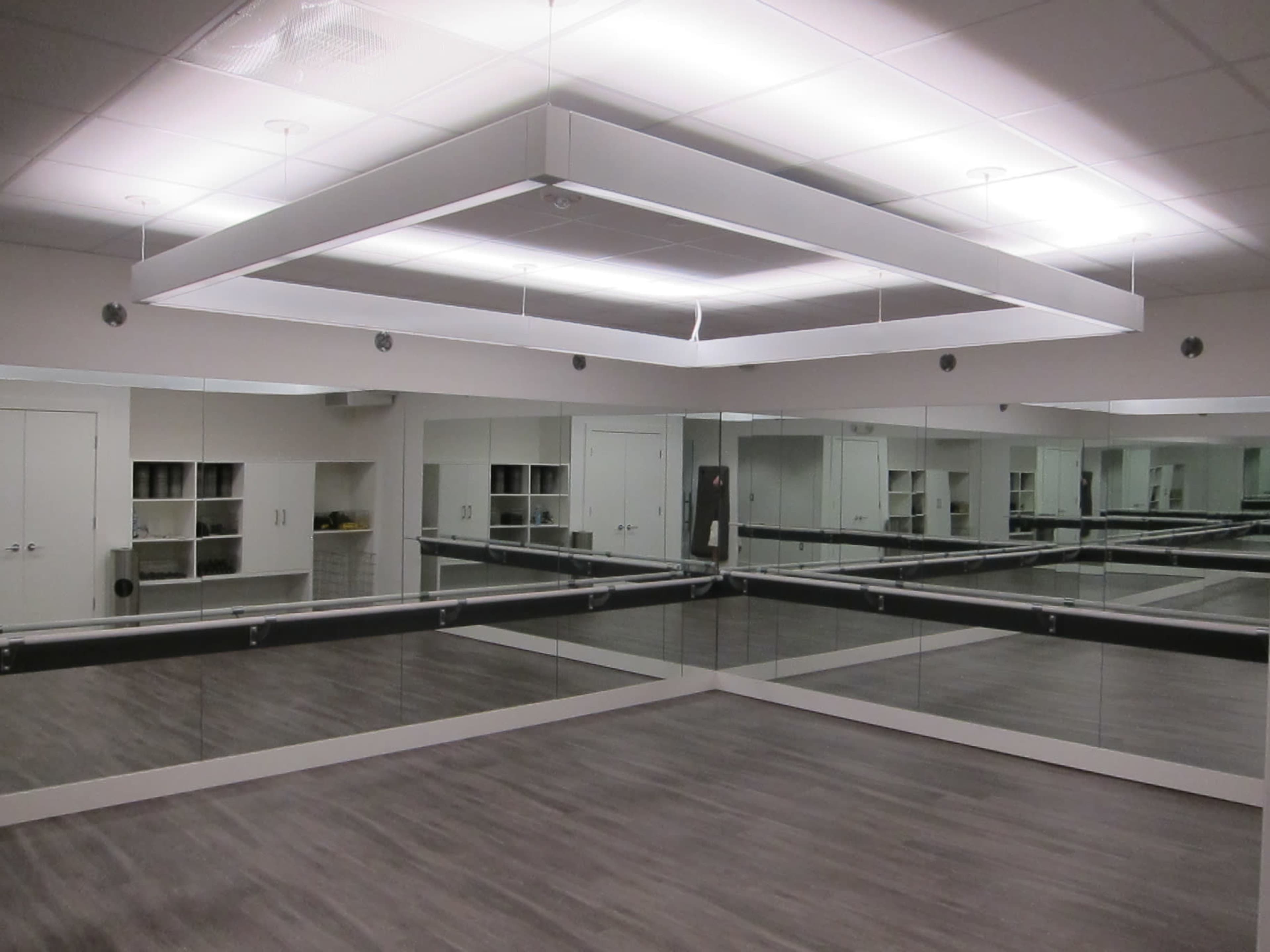 The image shows a mirrored dance studio with sleek wooden flooring and overhead lighting.