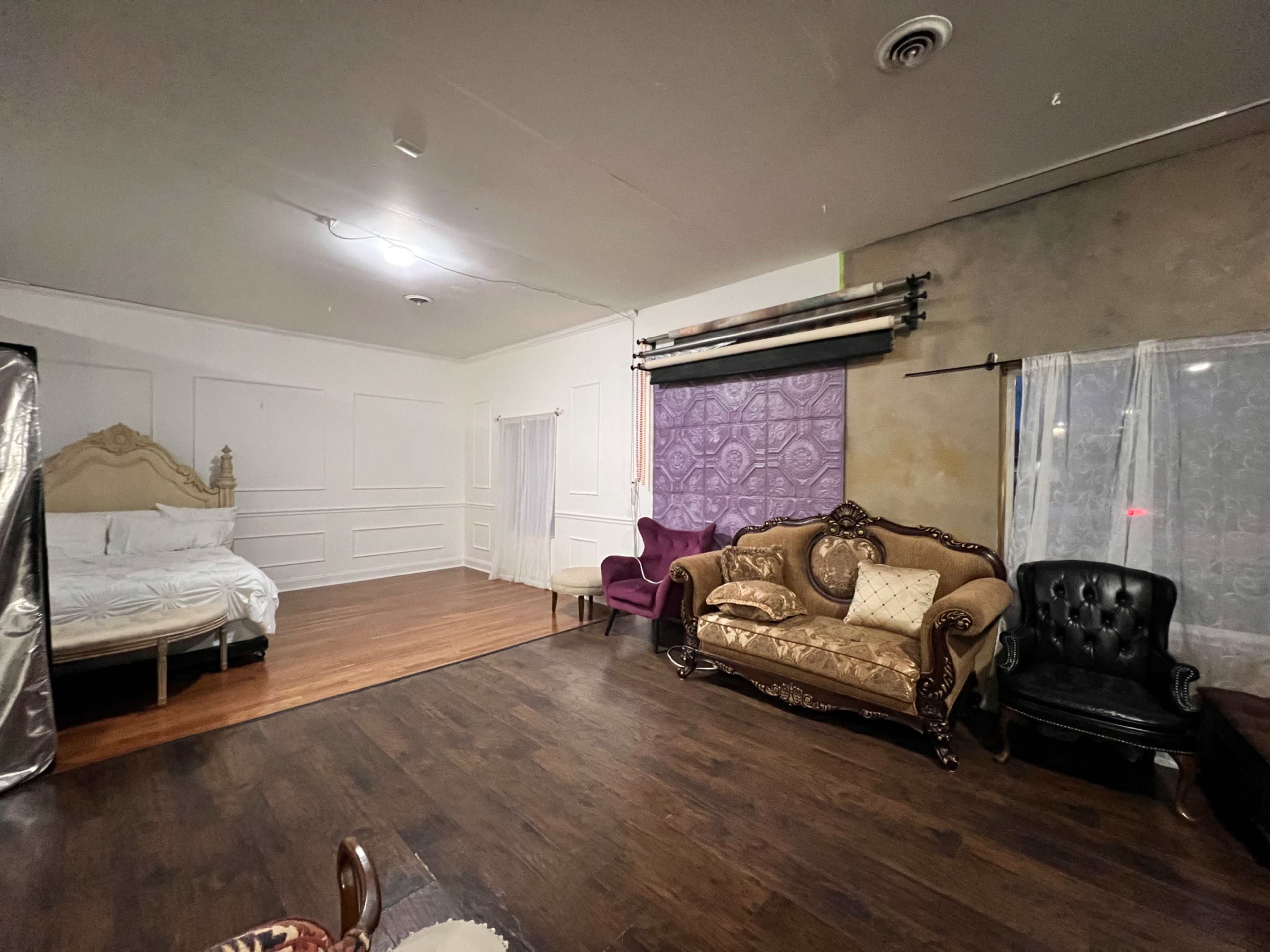 The image shows a spacious room with a bed on one side, a purple wall with a decorative pattern, and various sofas arranged in the seating area.