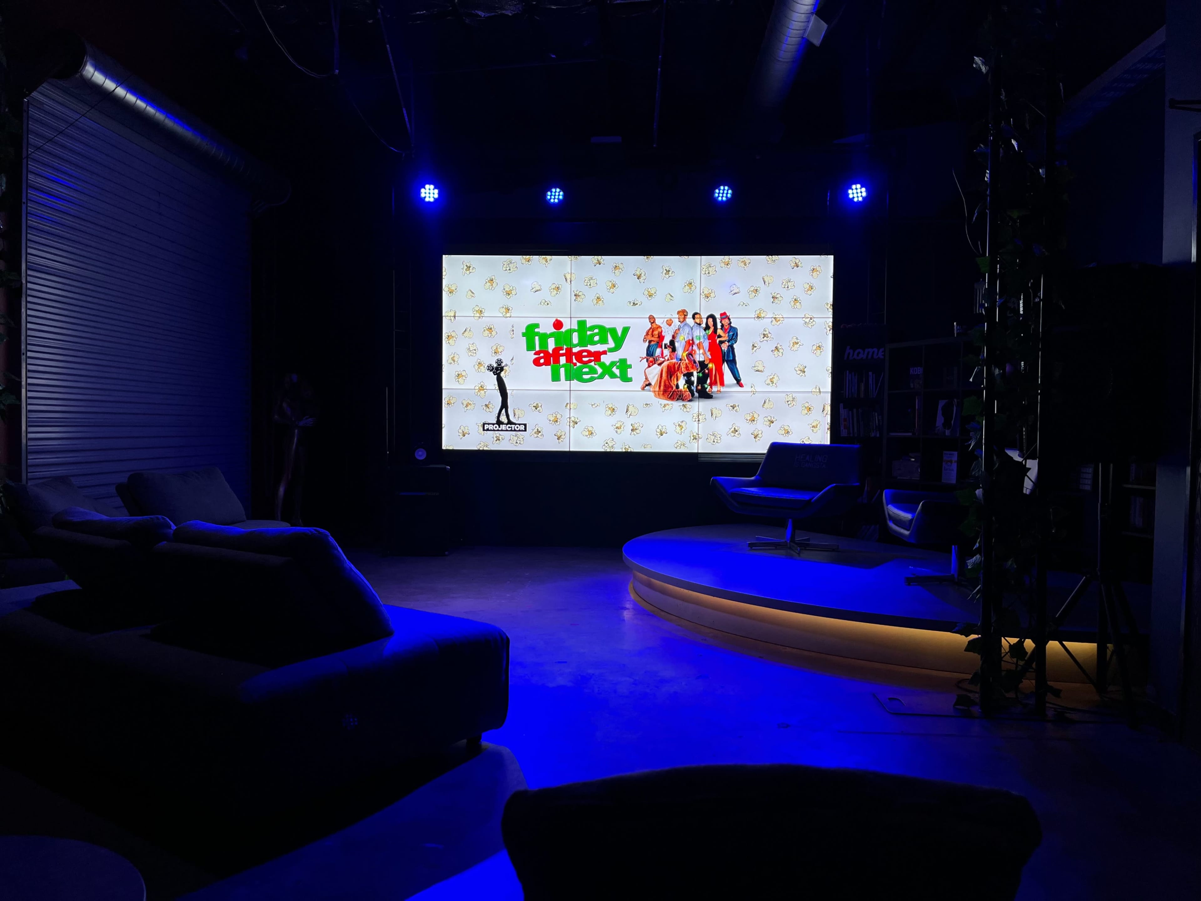 A large screen displays a promotional image for the movie "Friday After Next" in a dimly lit lounge area with seating.