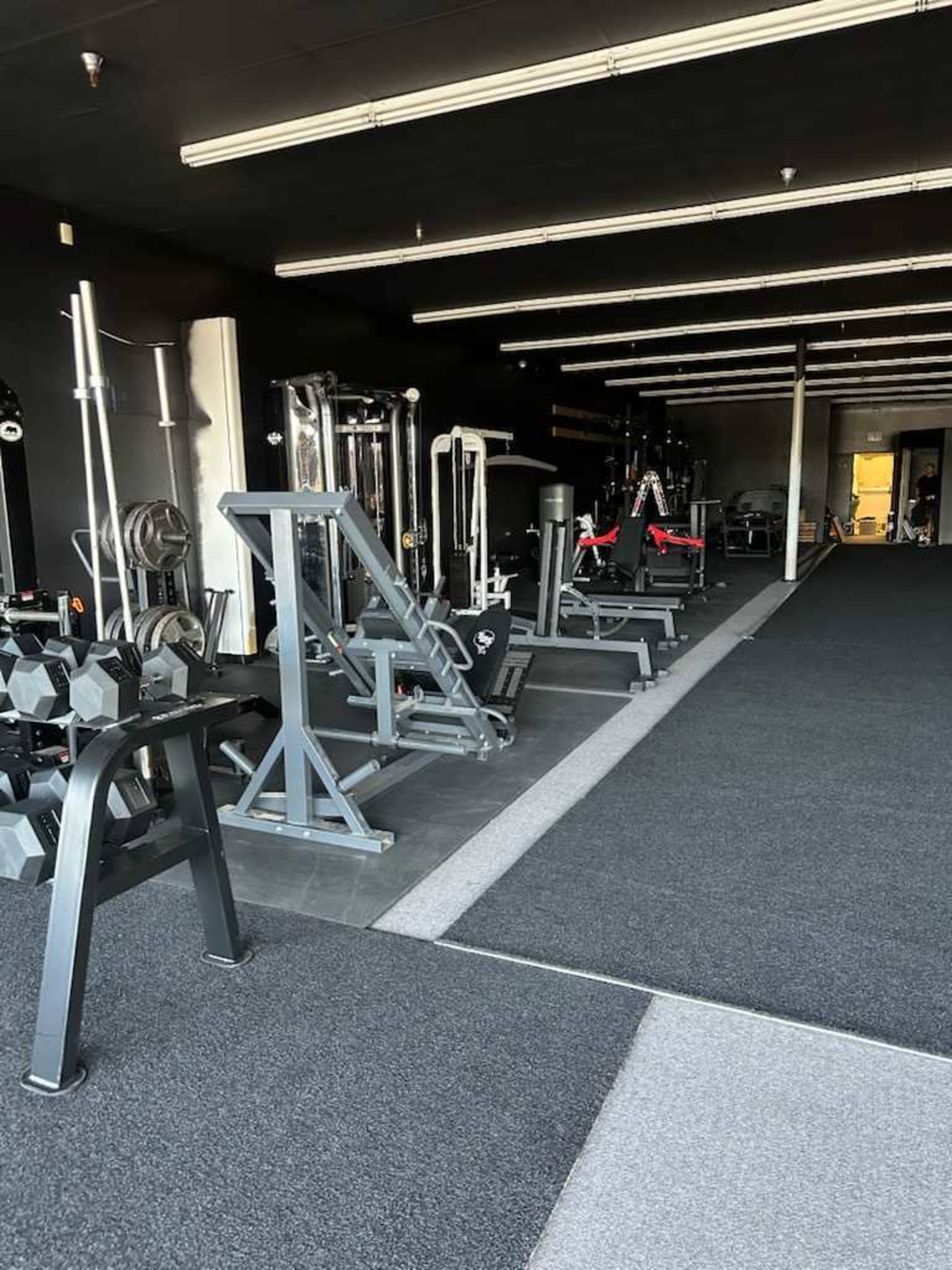 The image shows a well-equipped gym interior with various exercise machines and weights arranged neatly along the walls.