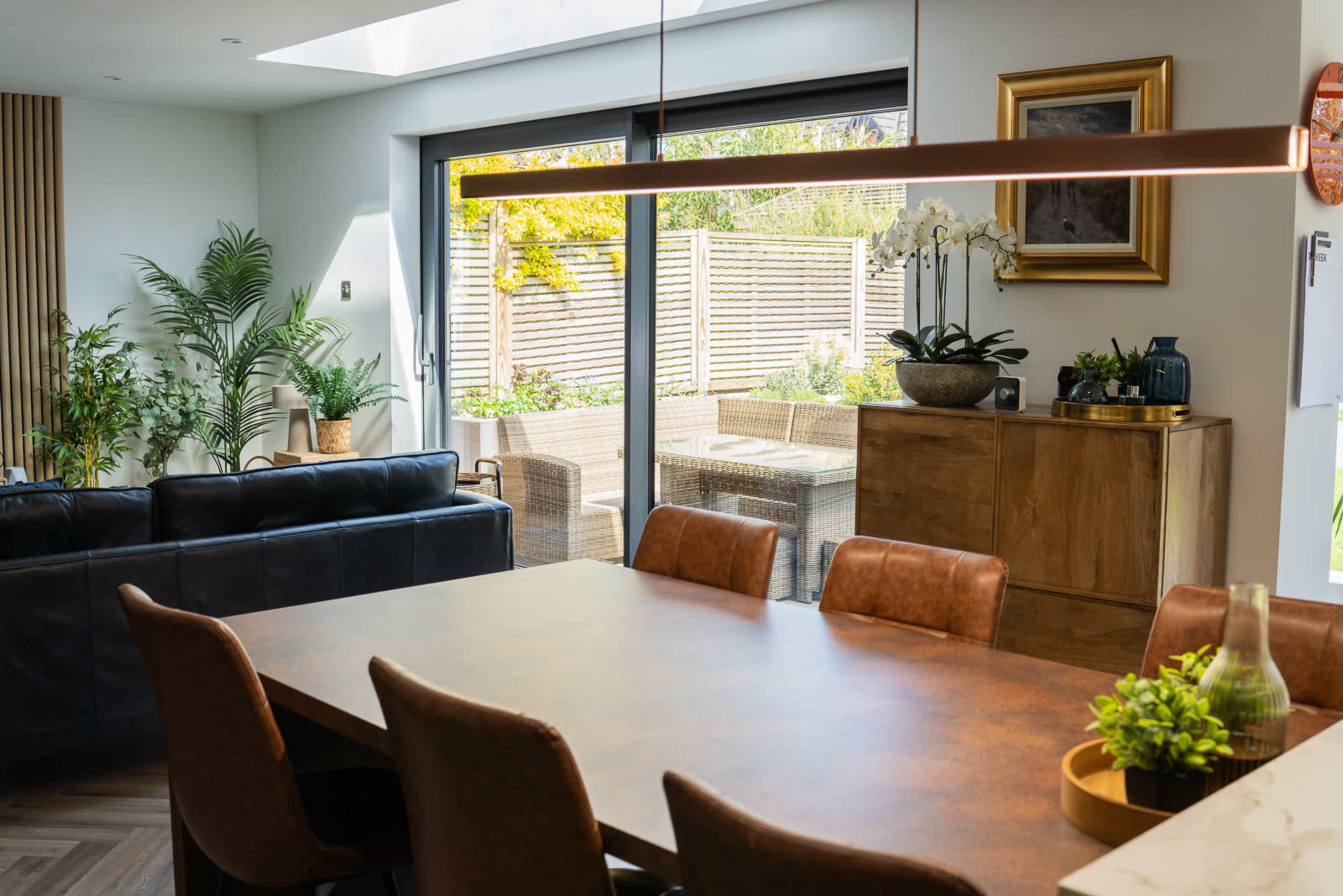 A dining area features a wooden table surrounded by brown leather chairs, with large glass doors leading to a well-groomed outdoor patio.
