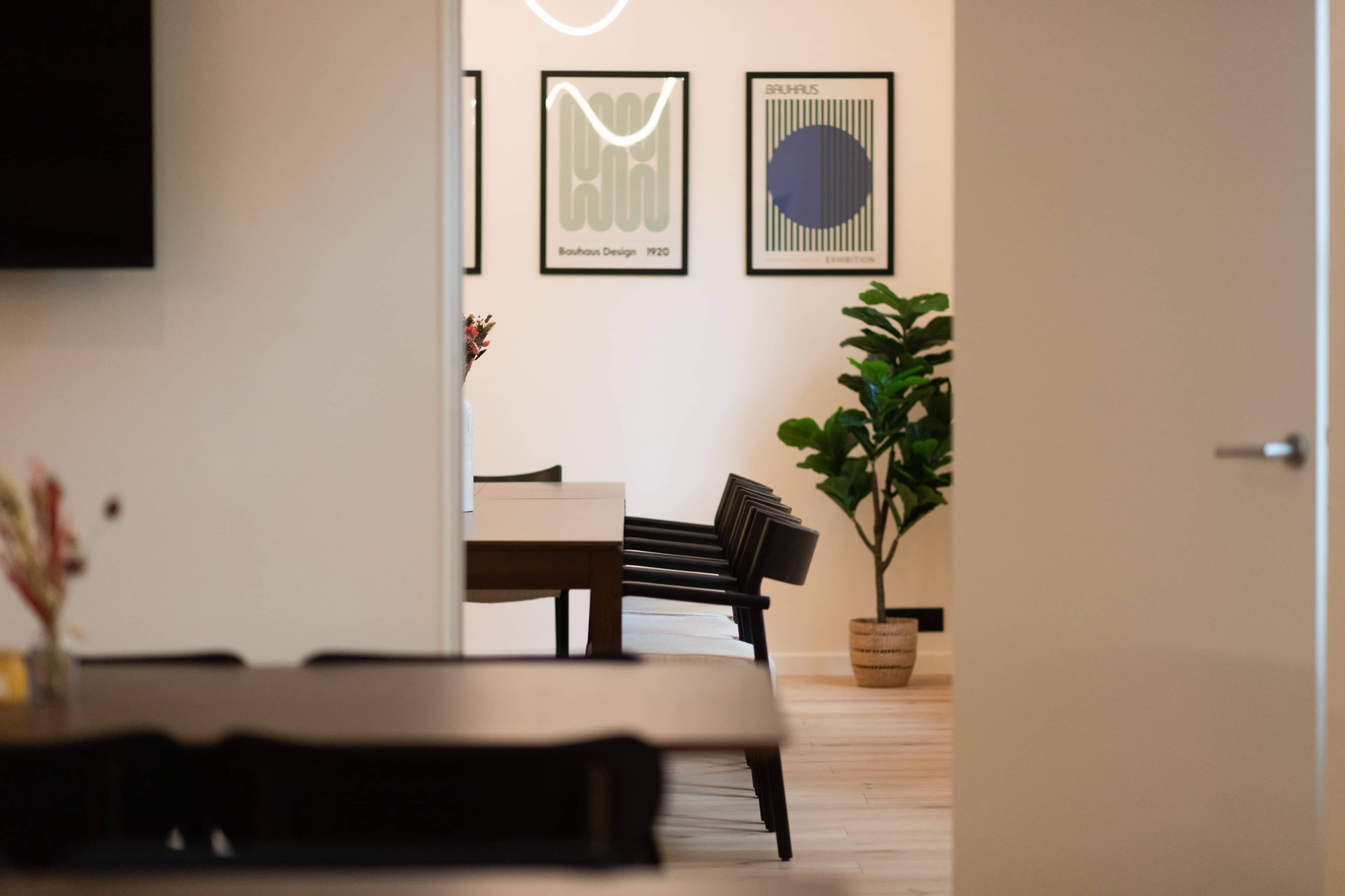 A modern interior space features a dining area with a table, chairs, and framed artwork on the walls, accompanied by a potted plant.