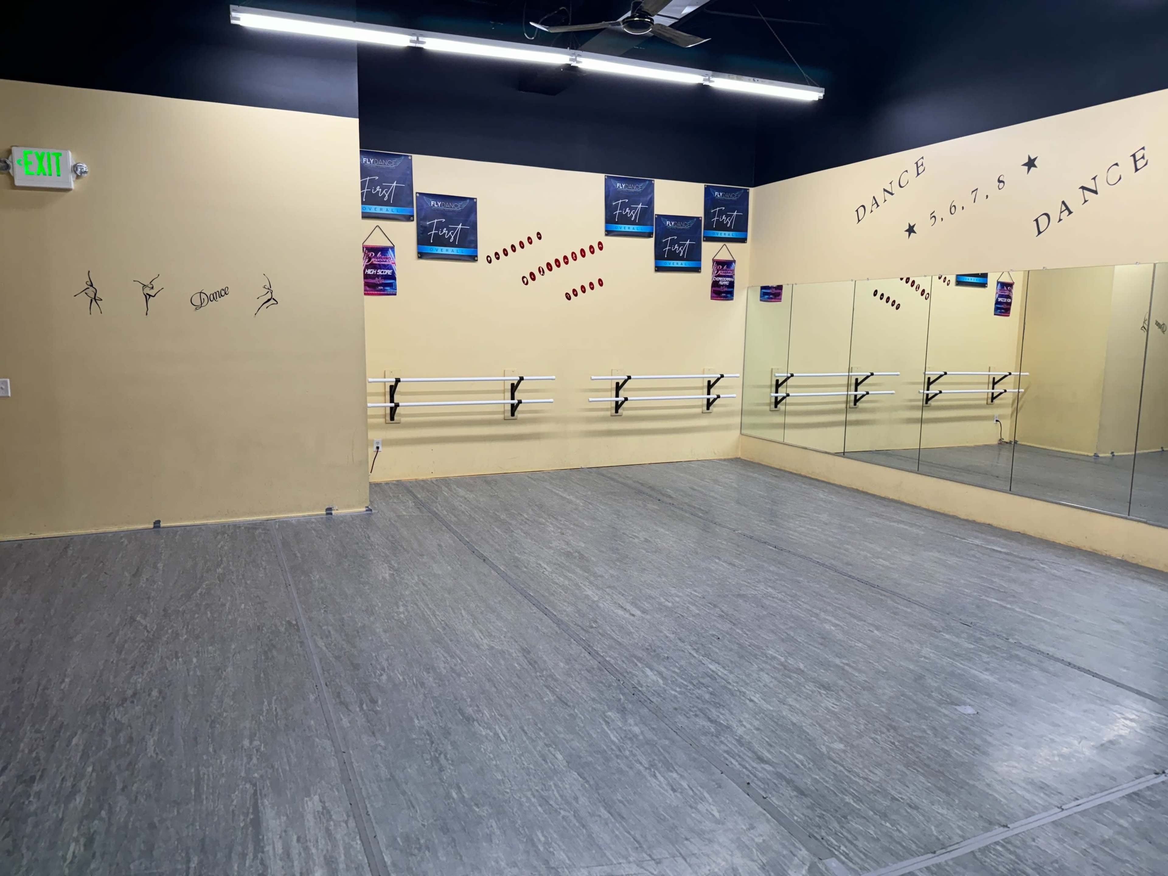 A dance studio with a wooden floor, wall mirrors, and decorations related to dance on the walls.