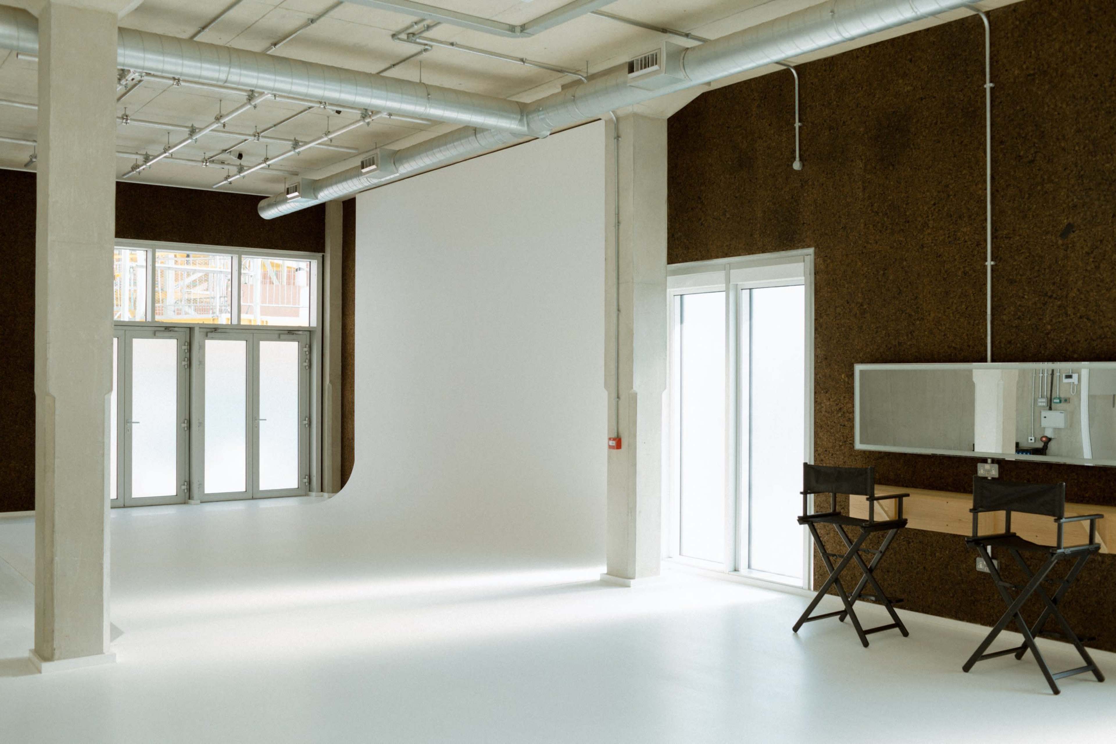 A spacious, well-lit studio with a large white backdrop, two director's chairs, and a mirror mounted on the wall.