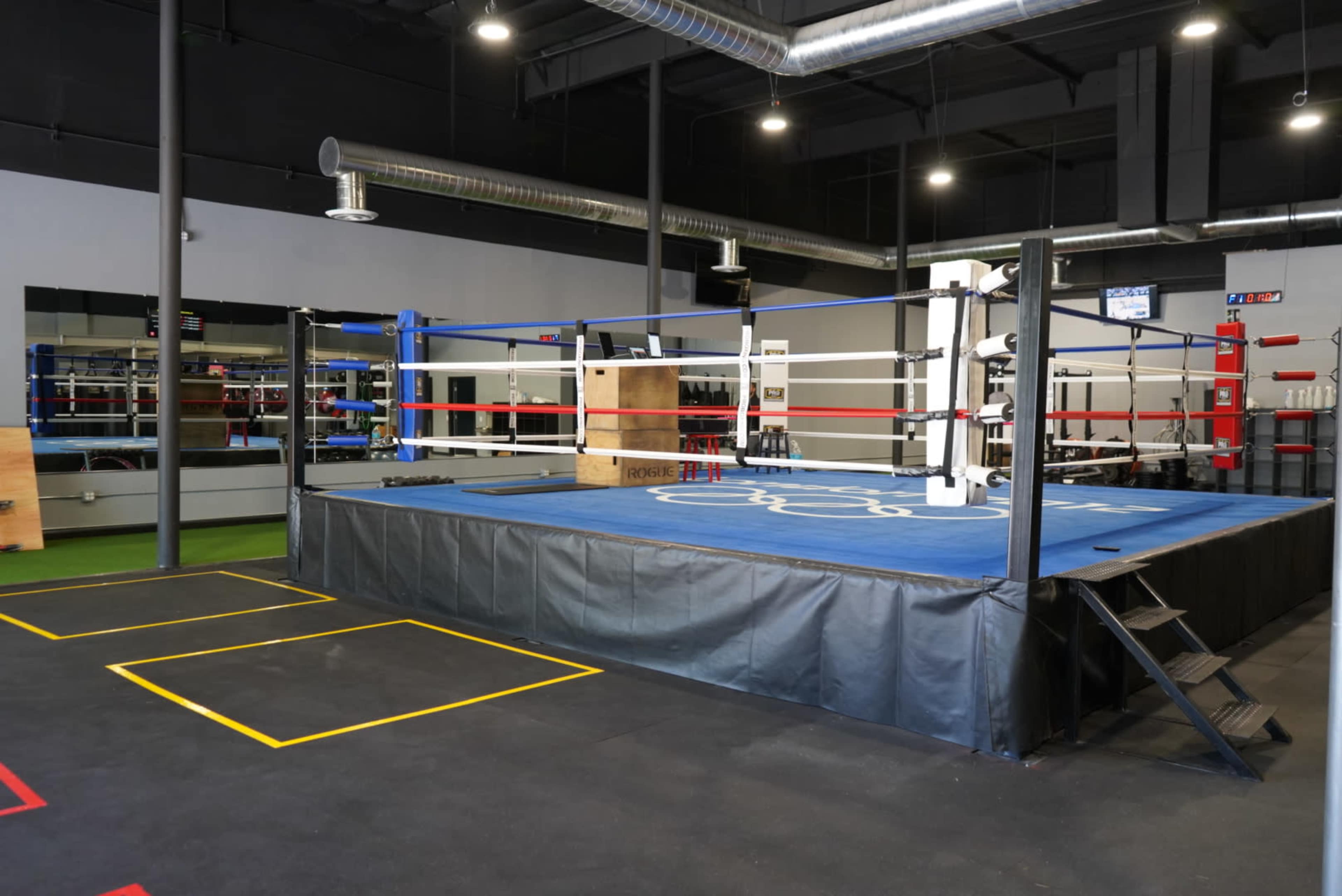 A professional boxing ring with blue and red corner posts set up in a training facility.