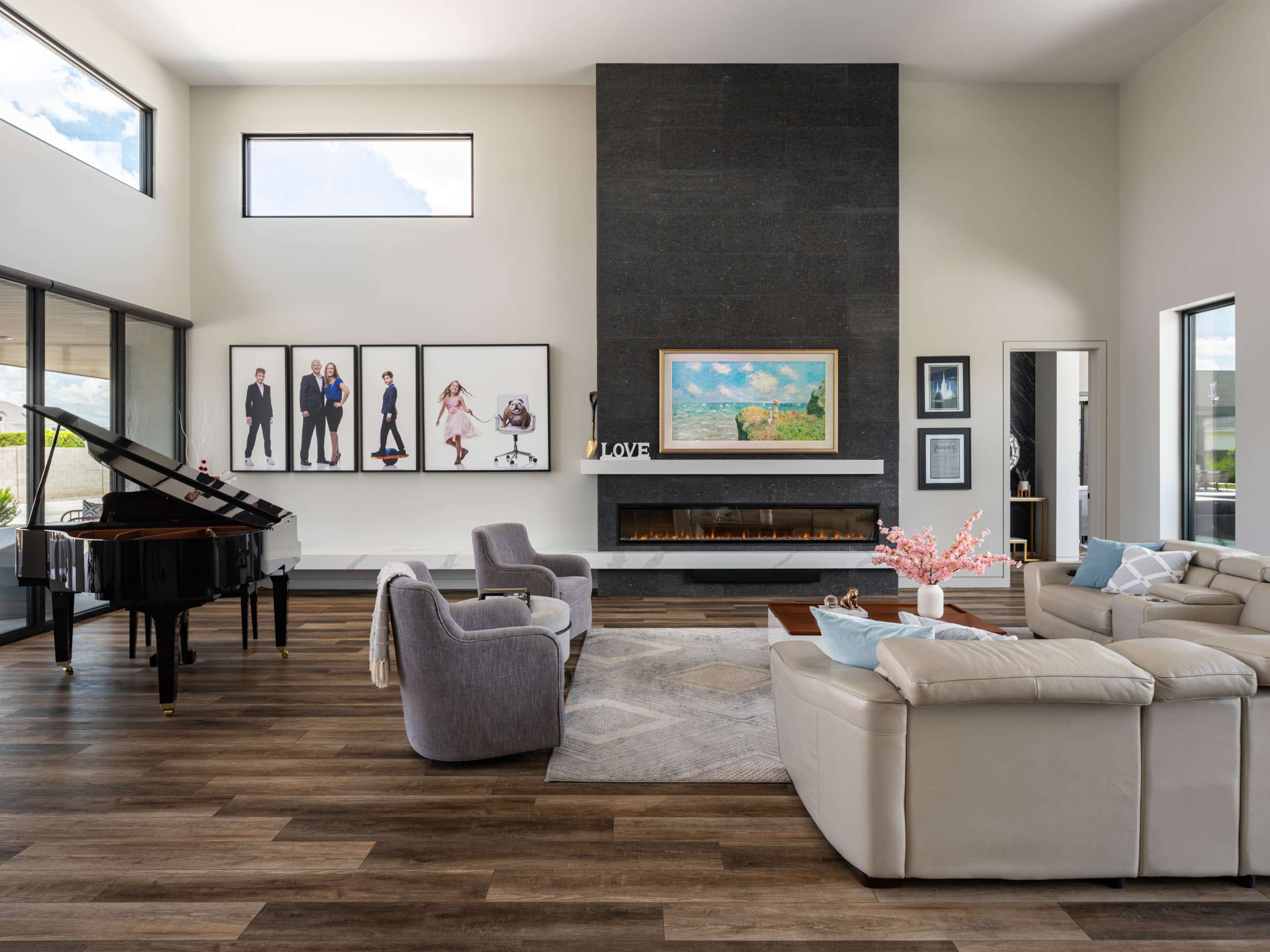 The spacious living room features a grand piano, modern furniture, and framed photographs on the walls, with a large window allowing natural light to fill the space.