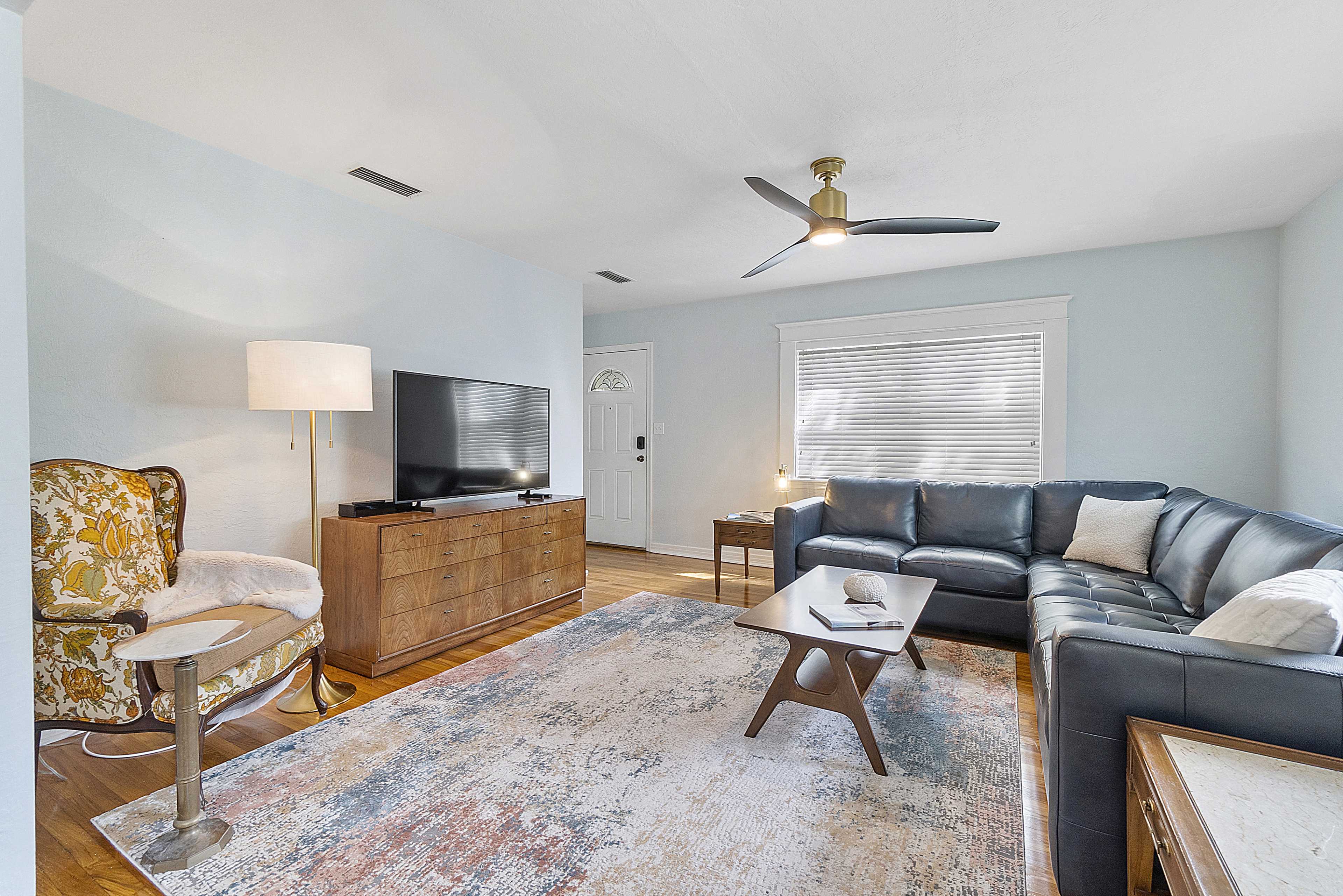 A well-furnished living room with a sectional couch, a wooden television stand, a coffee table, and large windows allowing natural light.