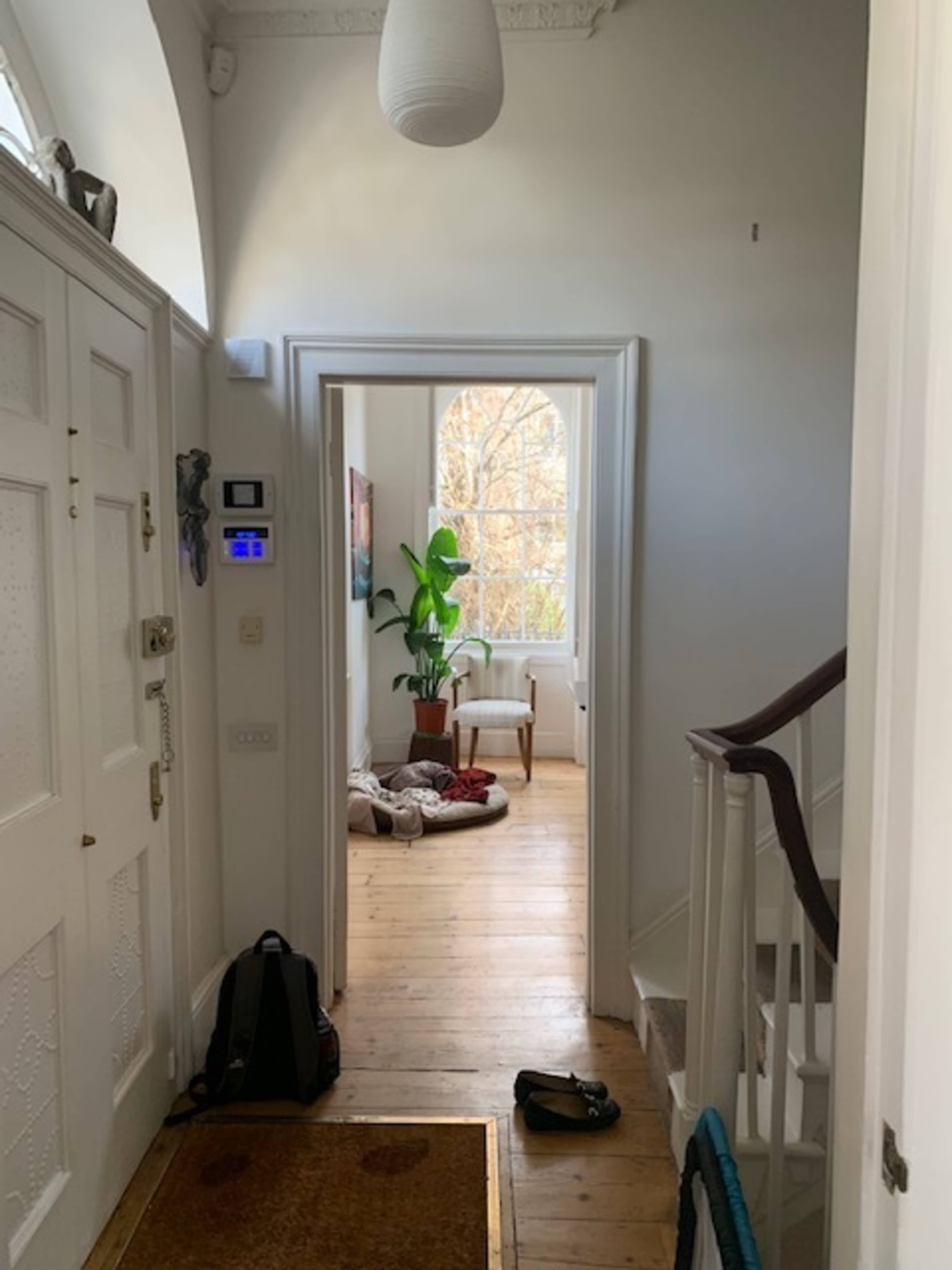 A hallway leads to a bright room with a large window and a potted plant, while a staircase is visible on the right.