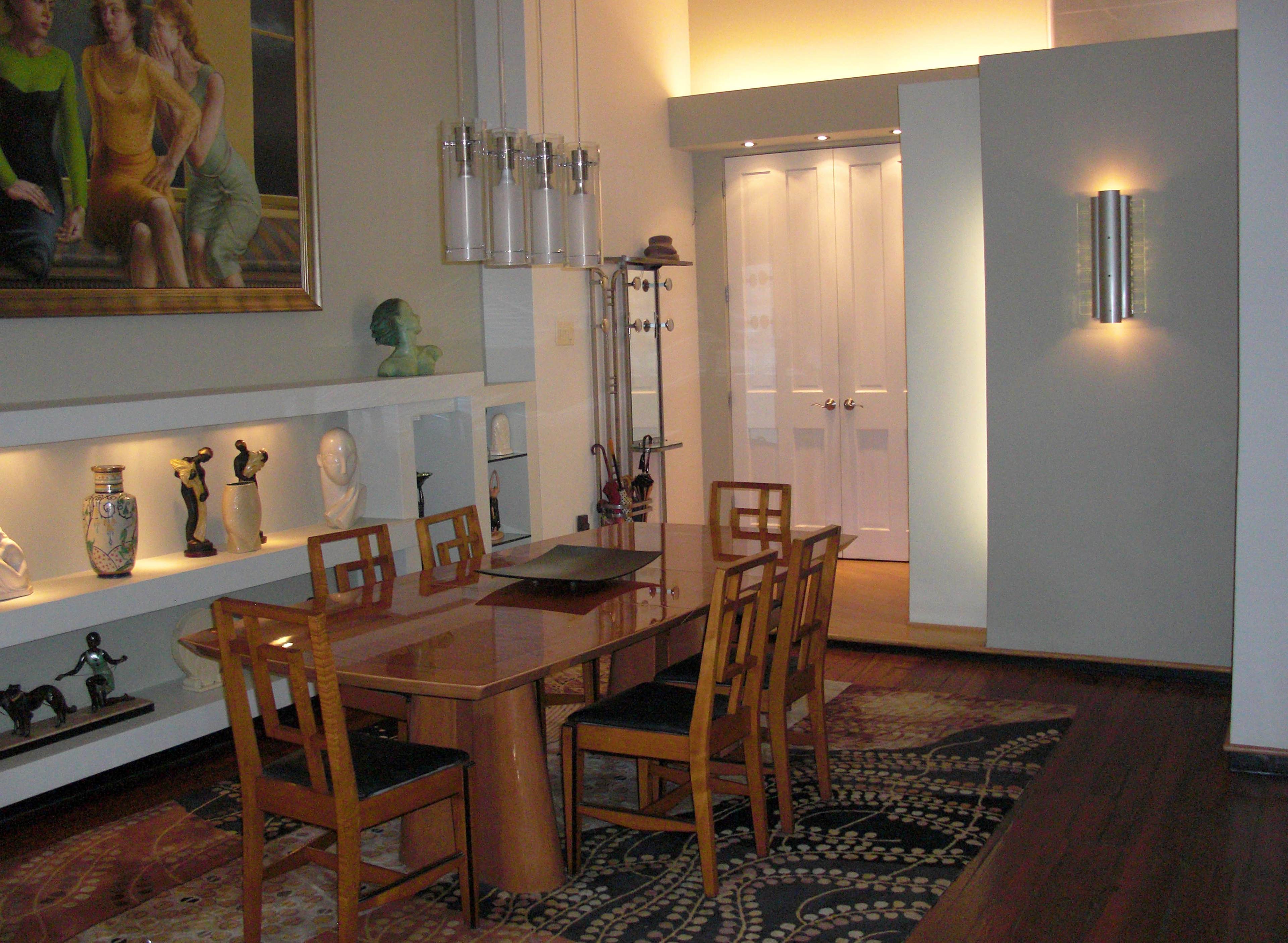 A modern dining room with a wooden table and six chairs, featuring decorative sculptures and a large painting on the wall.