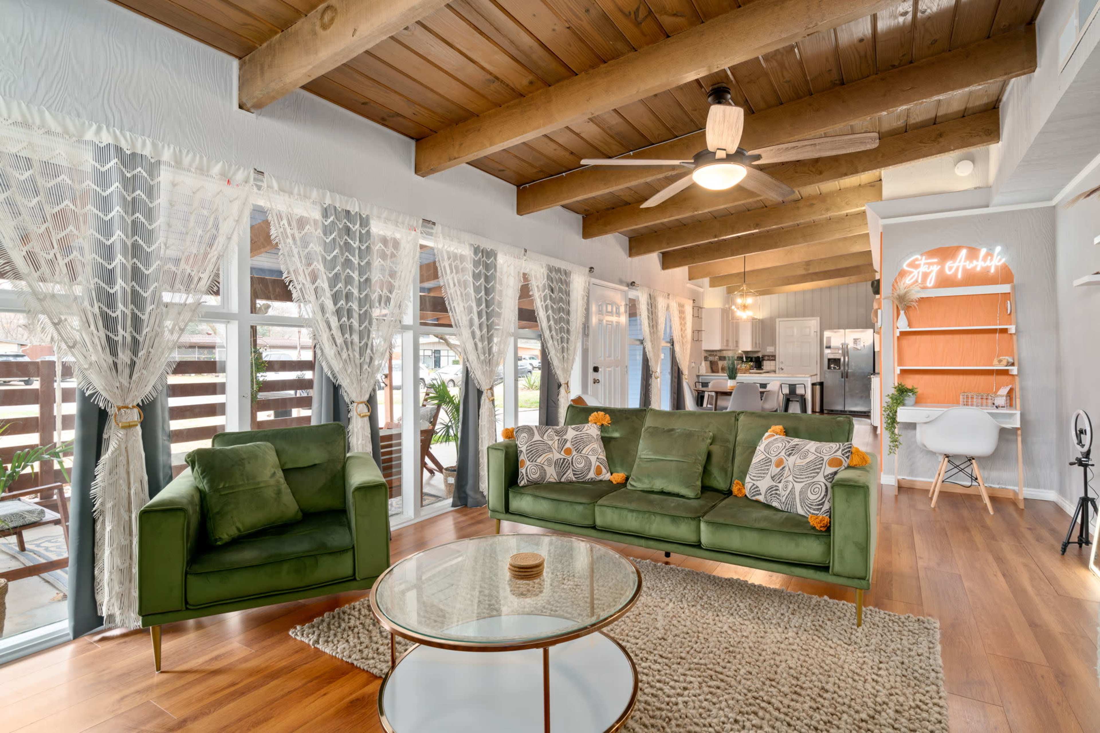 A bright living room with green sofas, wooden beams on the ceiling, and a round coffee table in front of large windows.