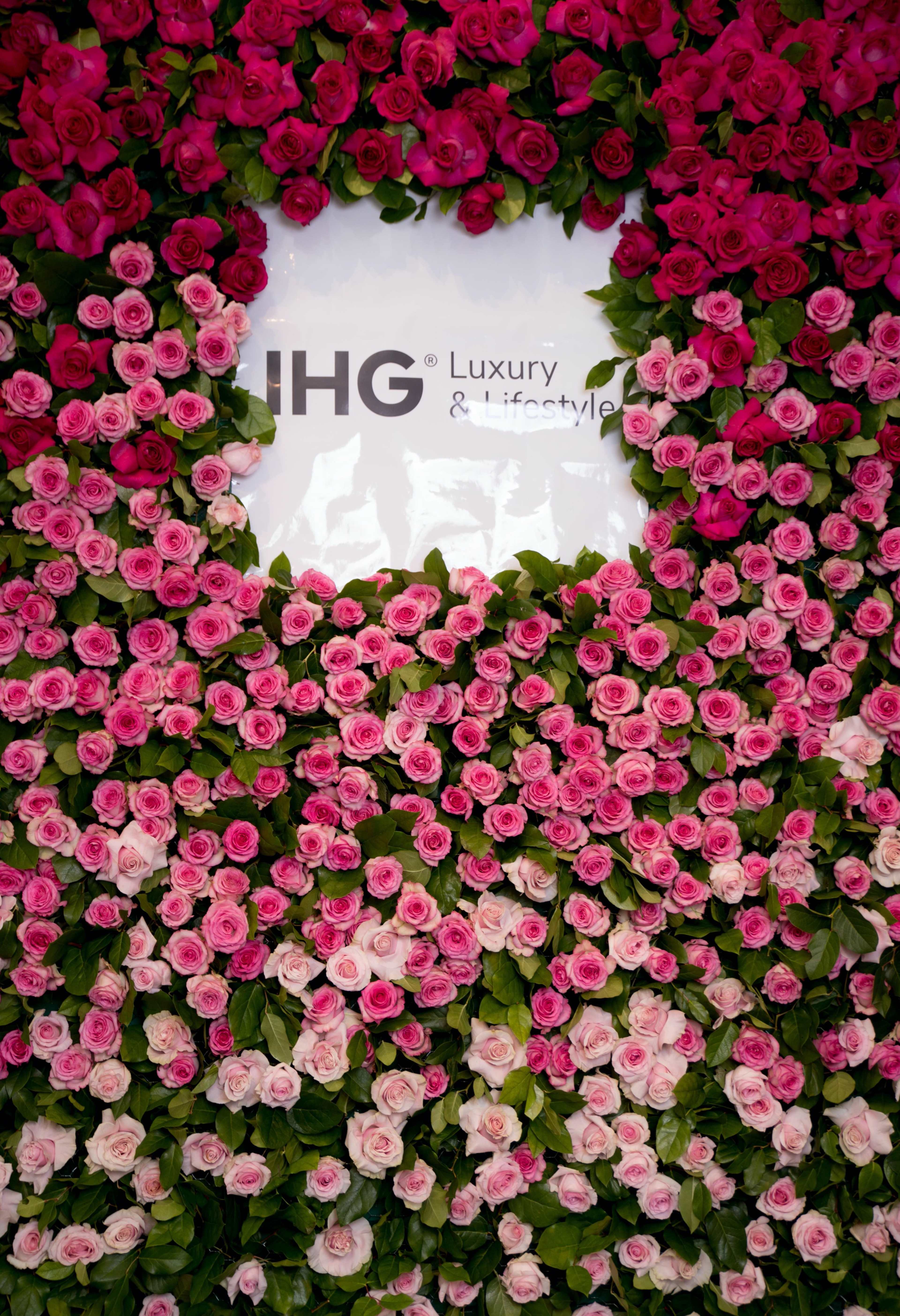 A wall covered with pink and white roses frames a sign for IHG Luxury & Lifestyle.