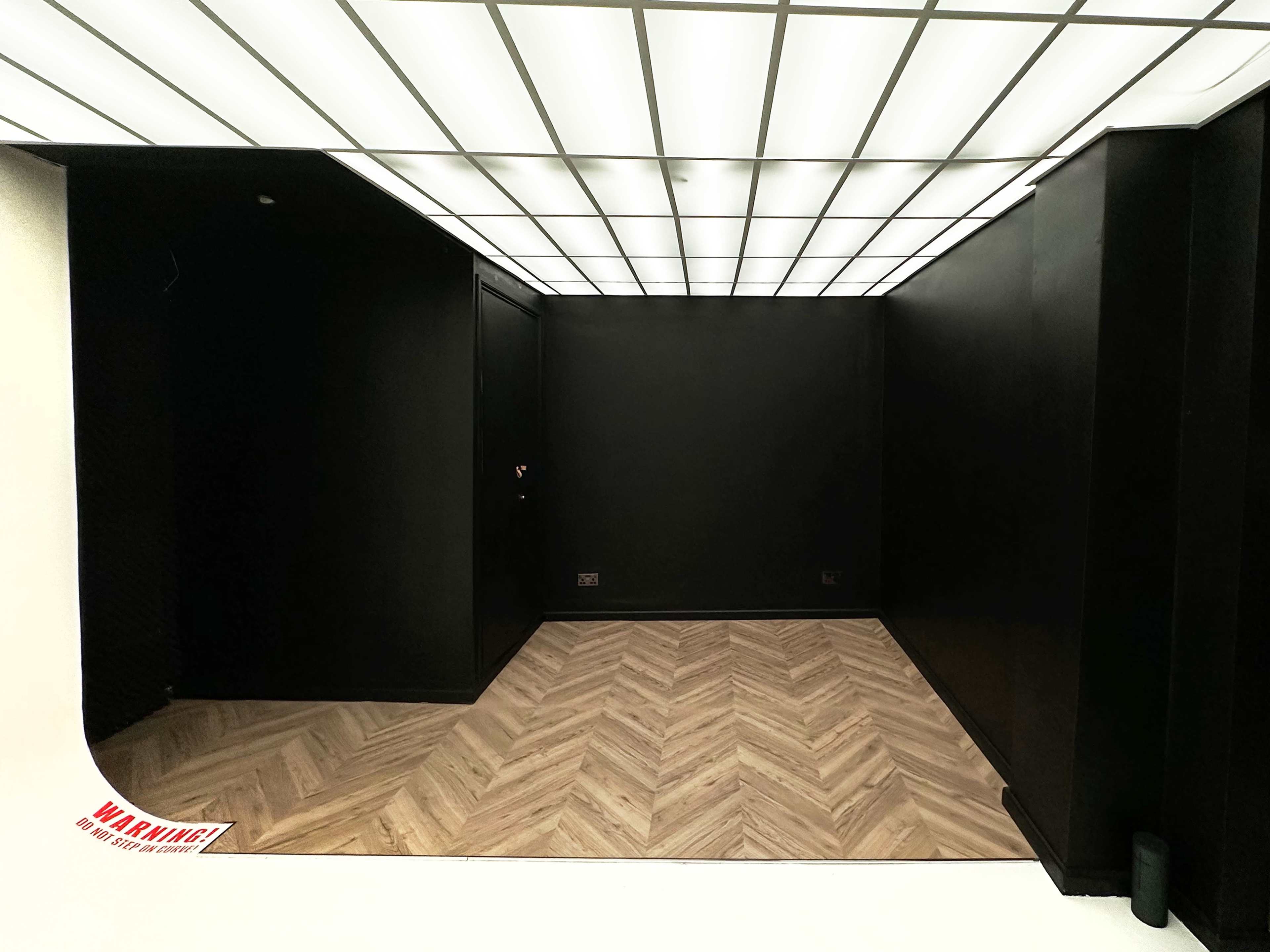 A black-walled room with a herringbone wooden floor and a ceiling of bright lights.