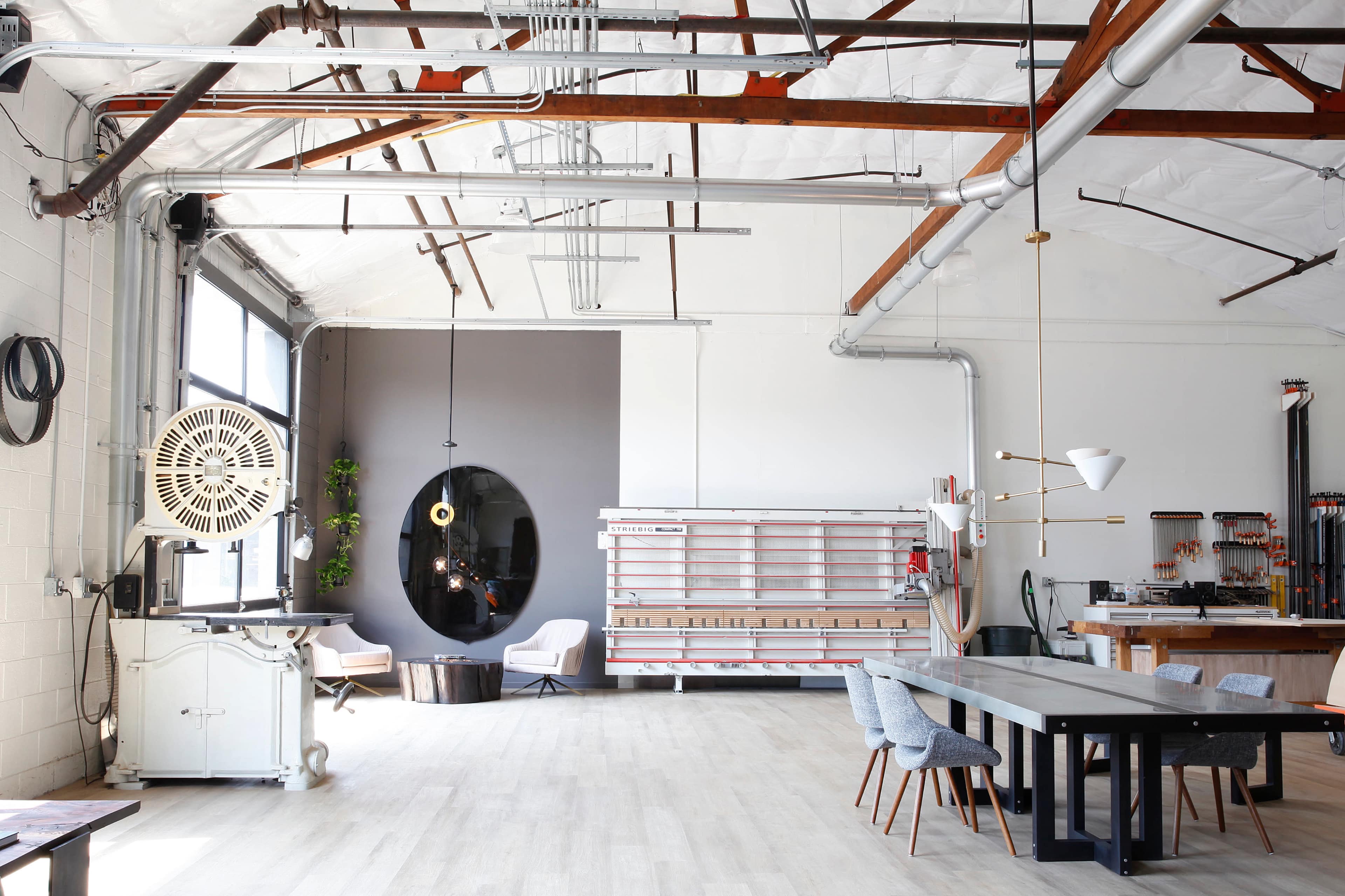 A spacious industrial-style interior with high ceilings, large windows, a mix of seating areas, and a long dining table.