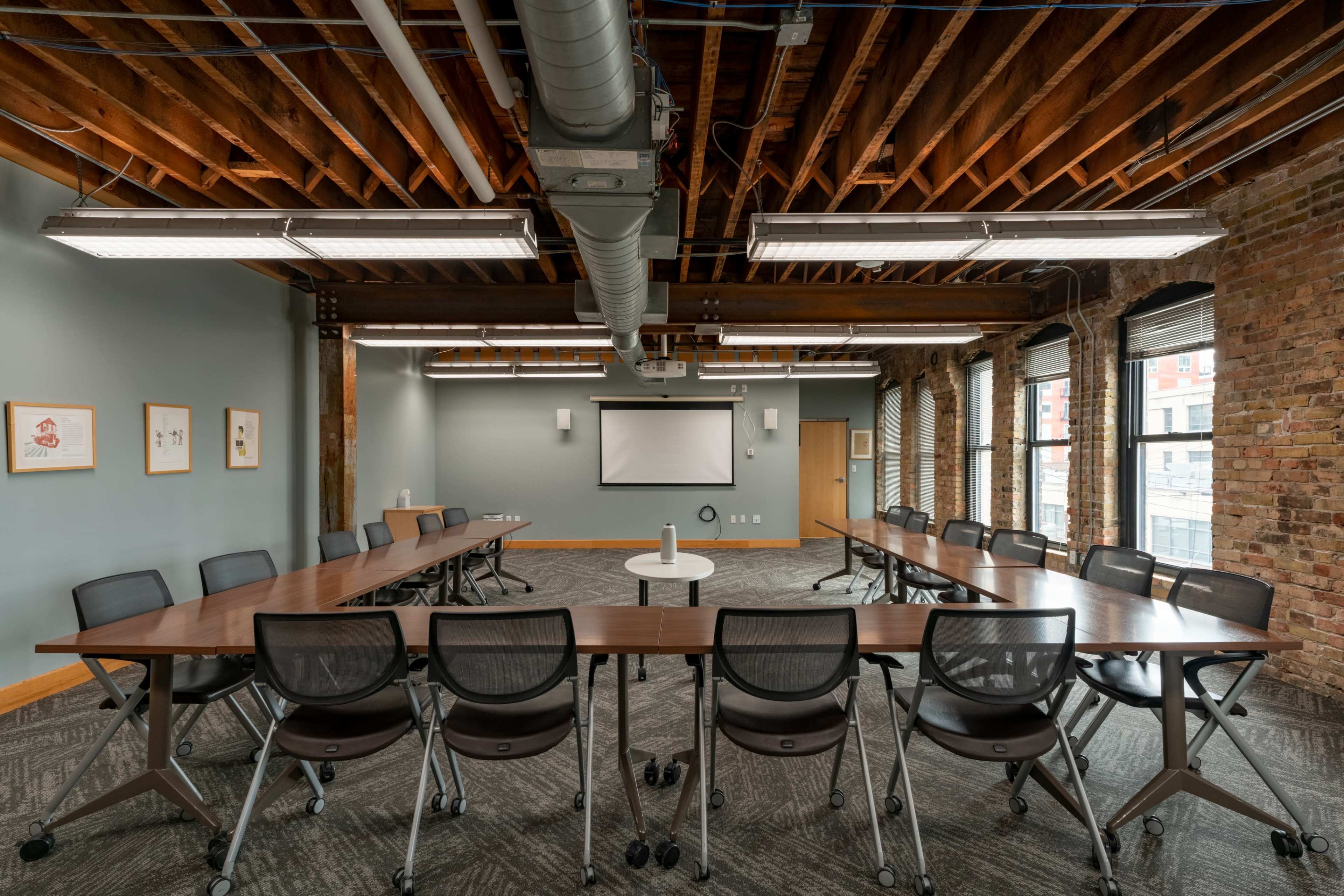 The image shows a spacious conference room with a large rectangular table surrounded by rolling chairs, exposed wooden beams, and large windows.