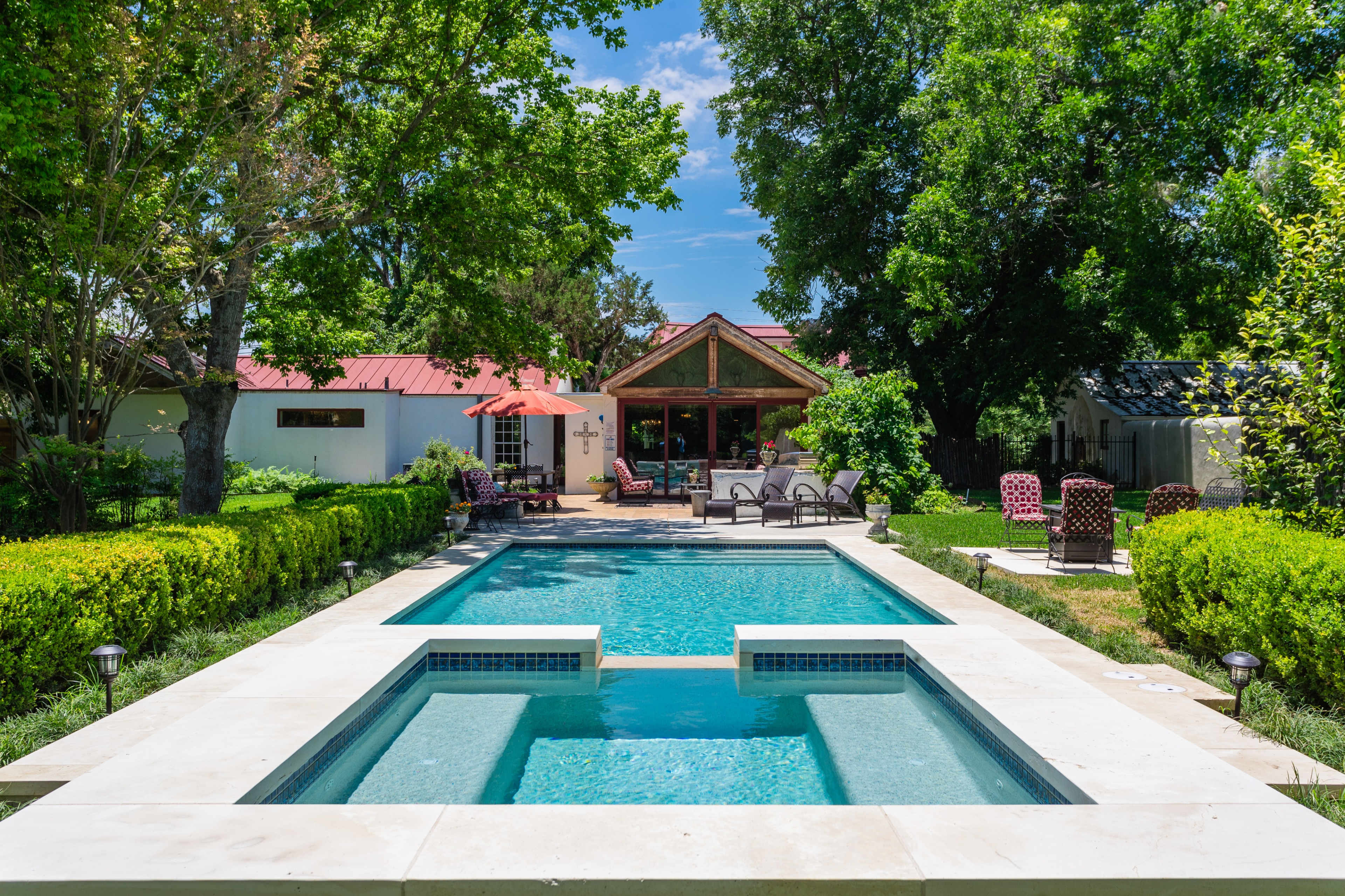 The image shows a backyard with a swimming pool surrounded by a landscaped garden and outdoor seating areas.
