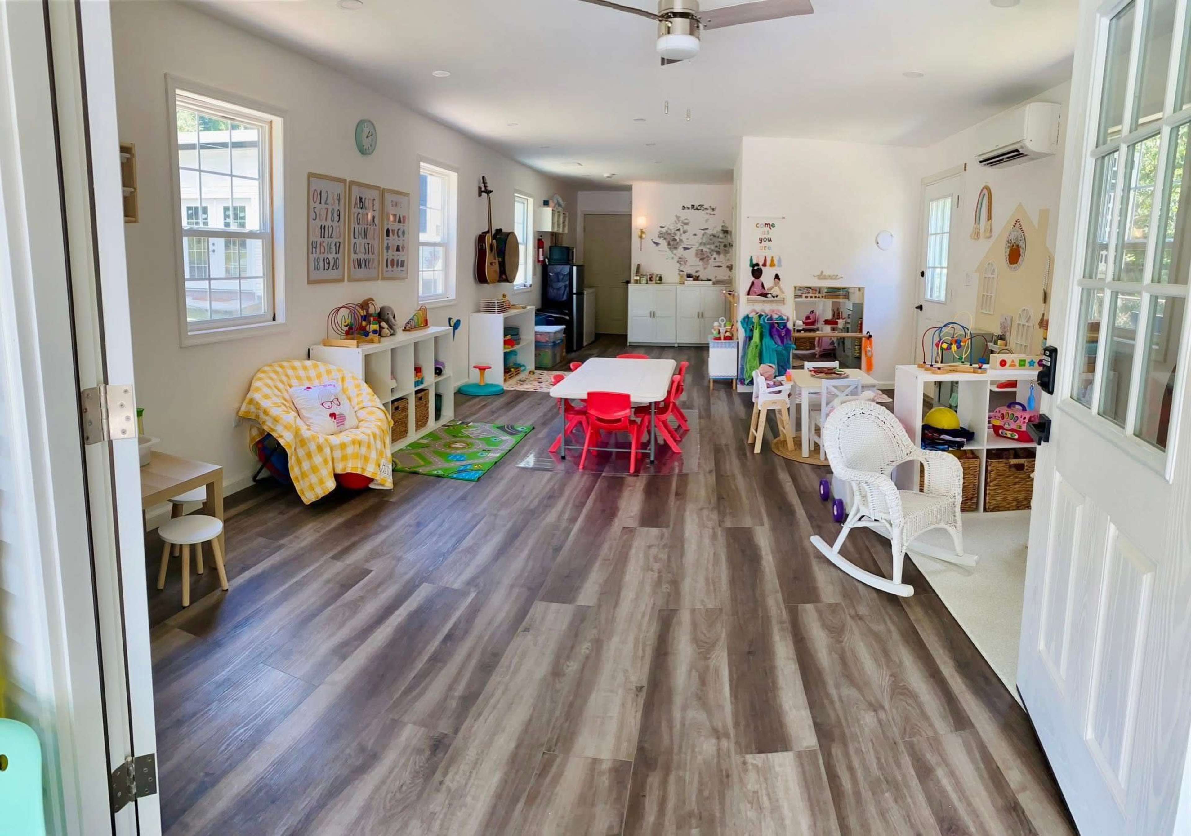The image shows a bright, open playroom filled with colorful toys, furniture, and areas for children's activities.