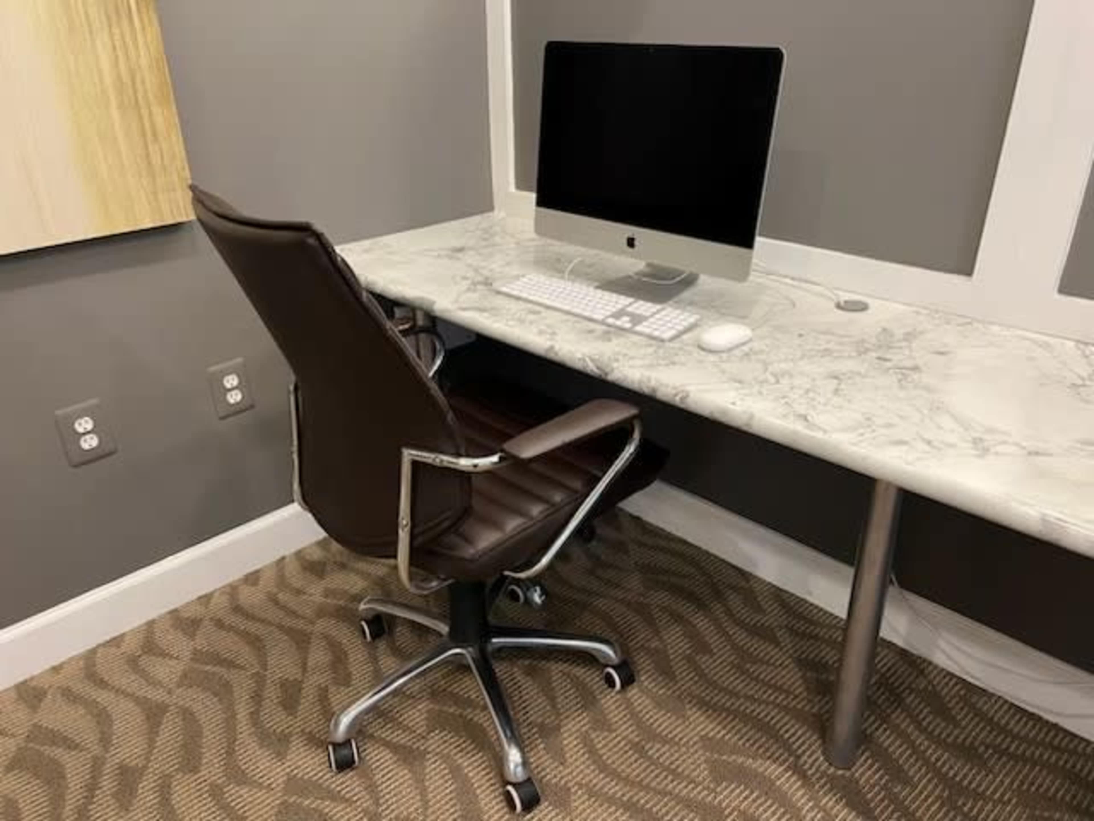 A sleek office setup features a marble desk with an iMac and a modern swivel chair against a gray wall.
