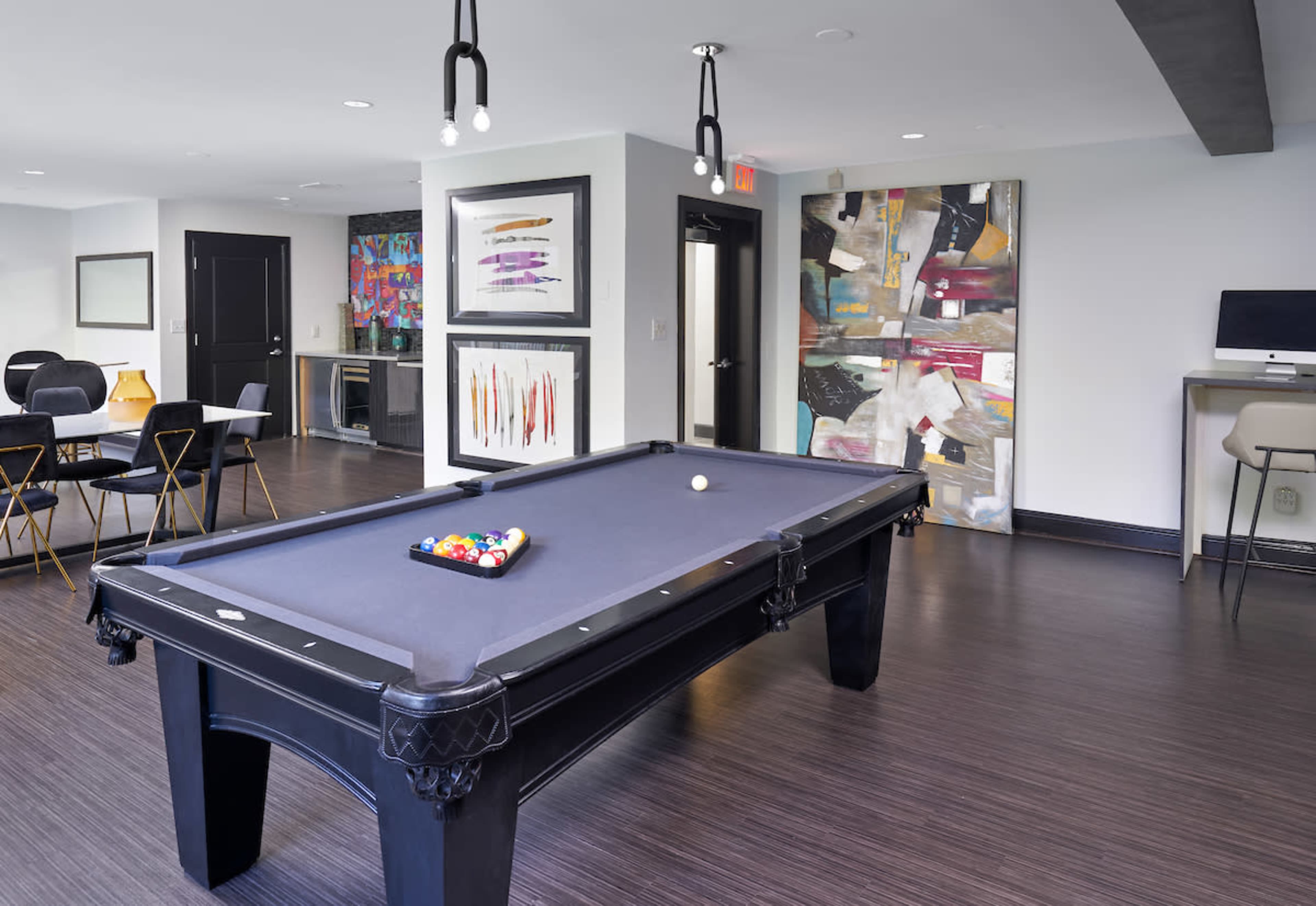 A modern game room featuring a black billiards table with colorful balls, surrounded by contemporary art and furniture.