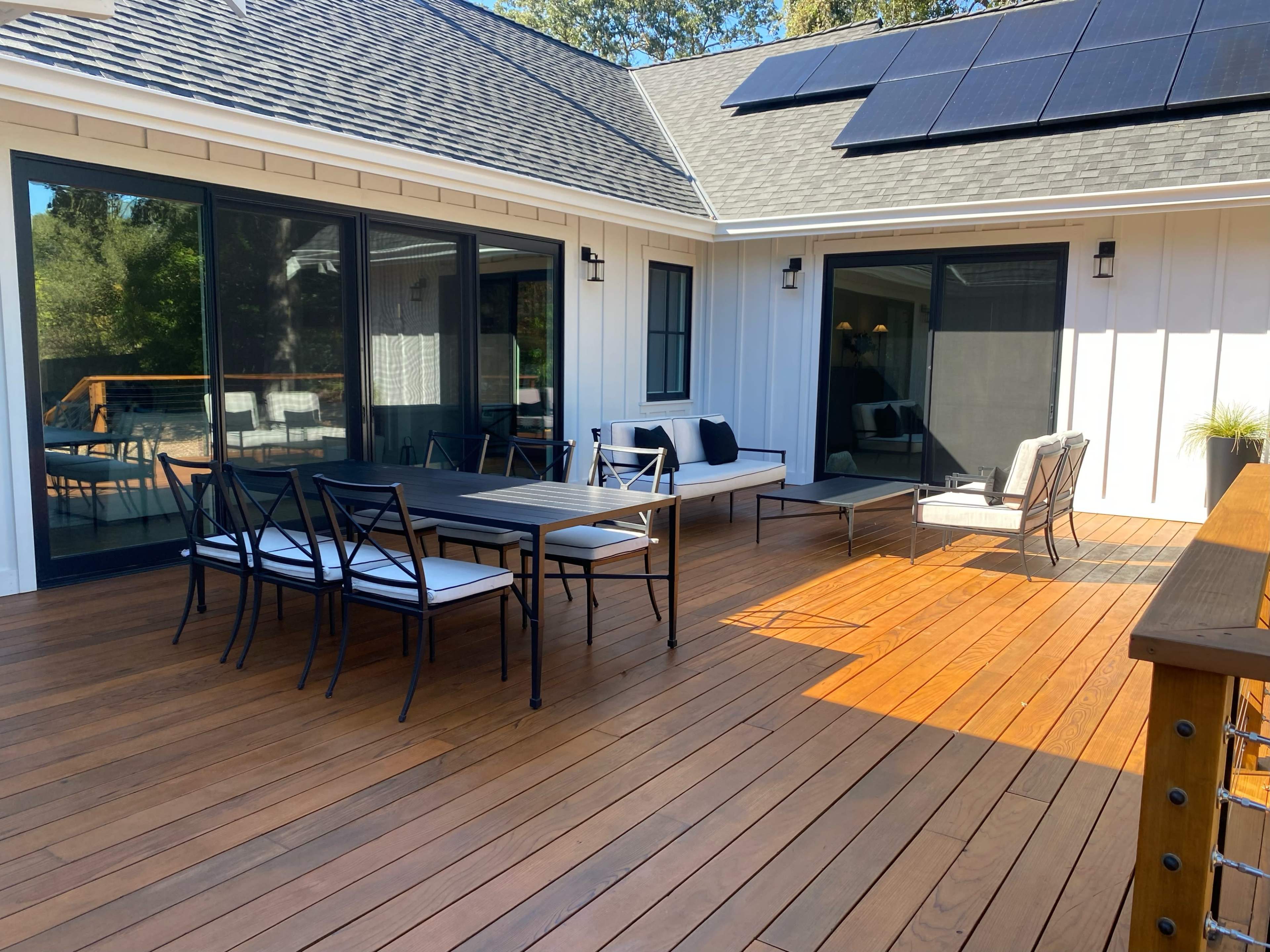 A spacious wooden deck featuring a dining table with seating for eight, lounge chairs, and solar panels on the roof.