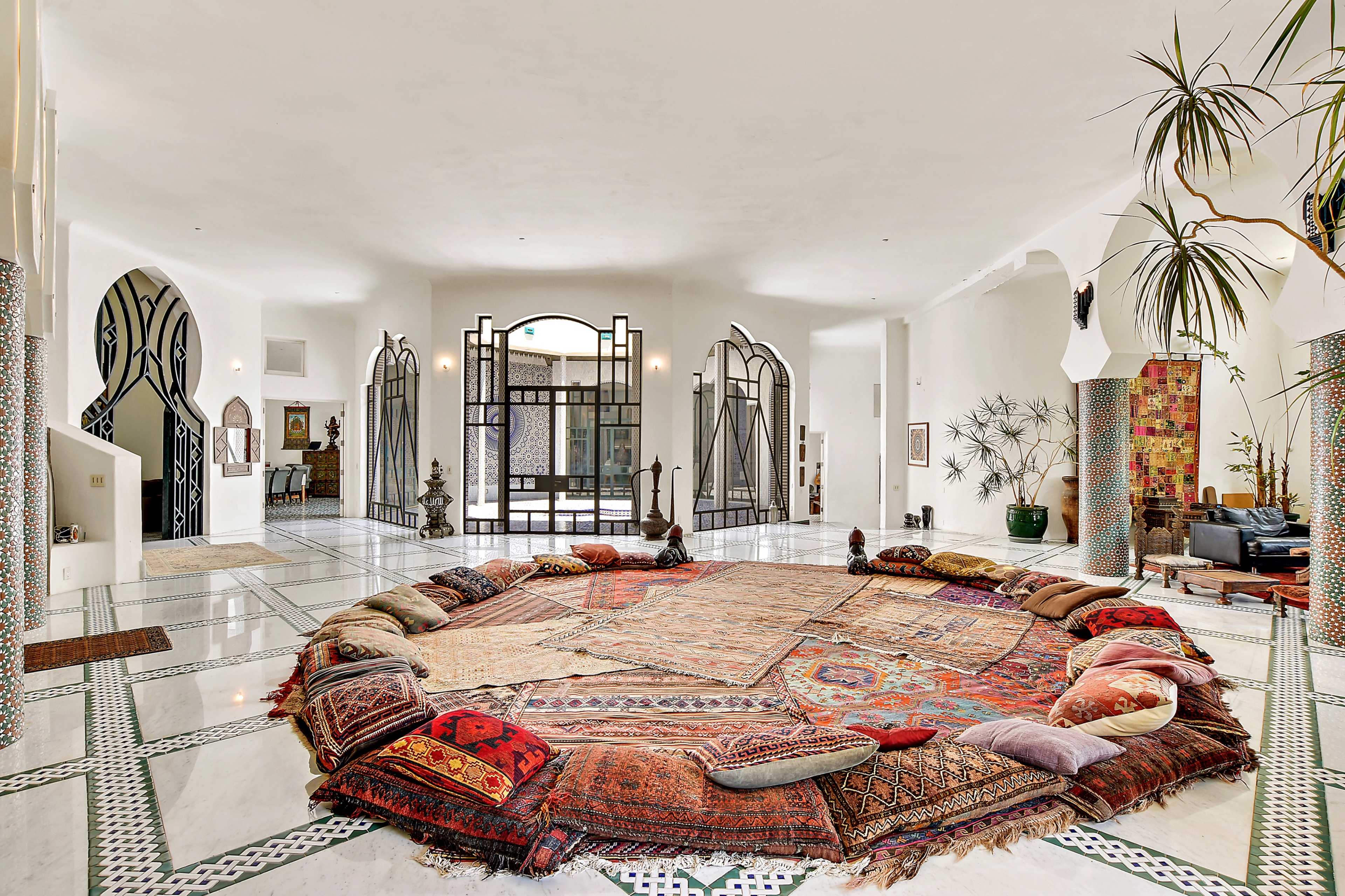 The image displays a large, circular seating area filled with colorful floor cushions surrounded by a spacious, brightly lit room with intricate architectural details.