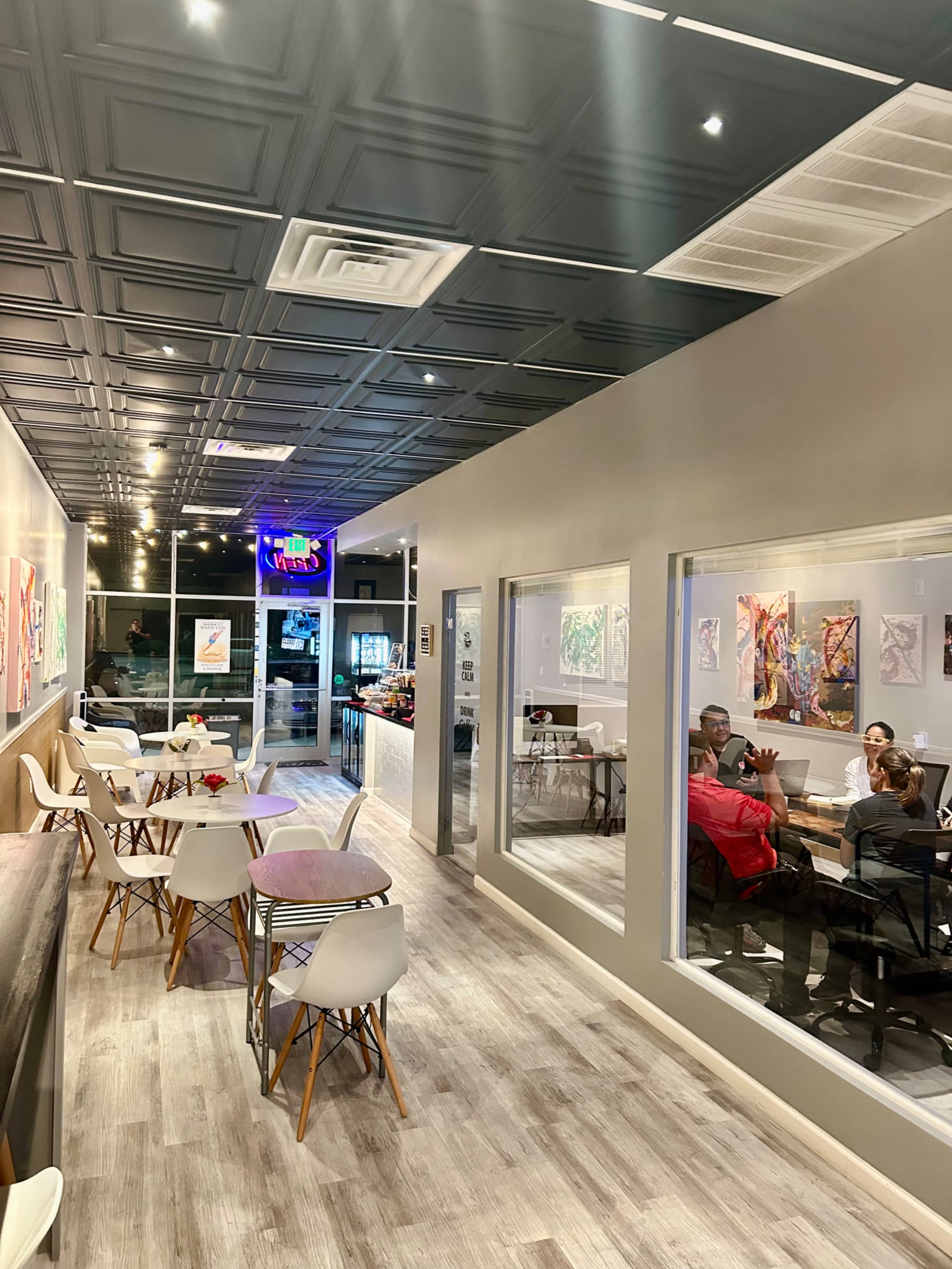 The image shows a modern café interior with a long hallway, seating areas on both sides, and large windows showcasing the outdoor view.