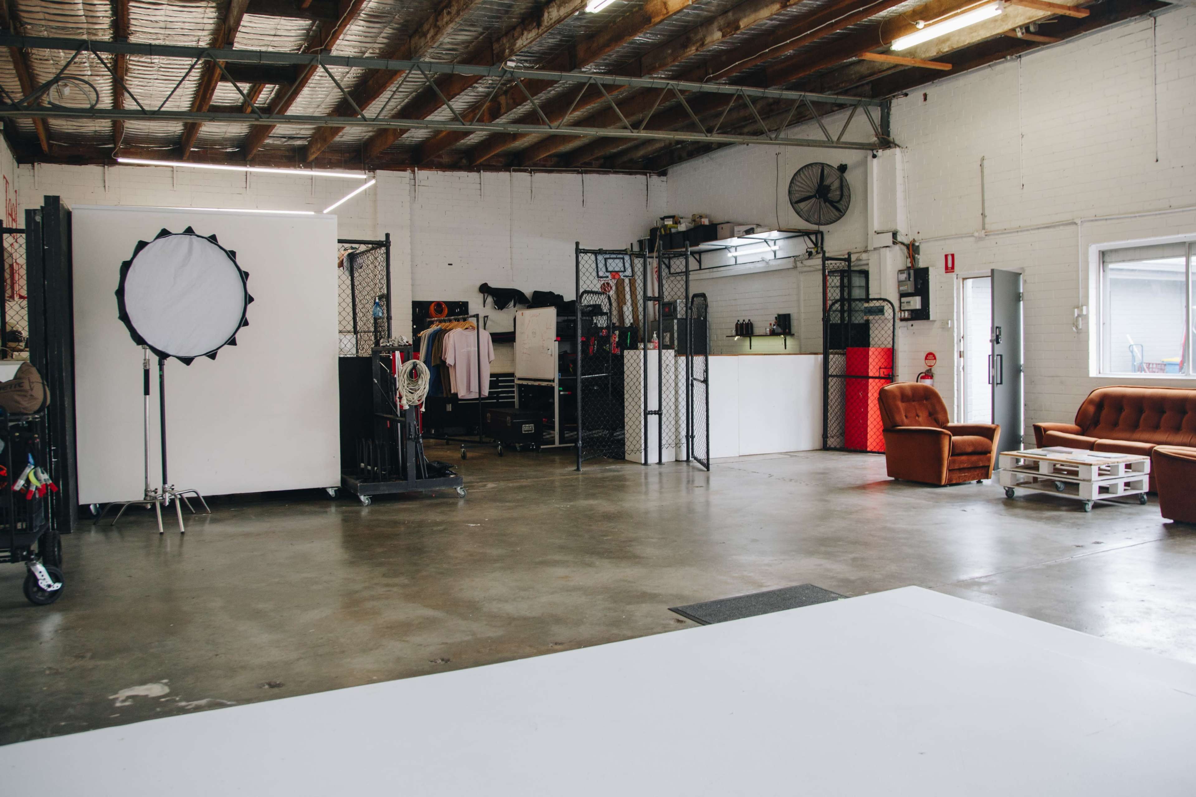 A spacious interior of a photography studio with a large white backdrop, a few furniture pieces, and various equipment organized along the walls.