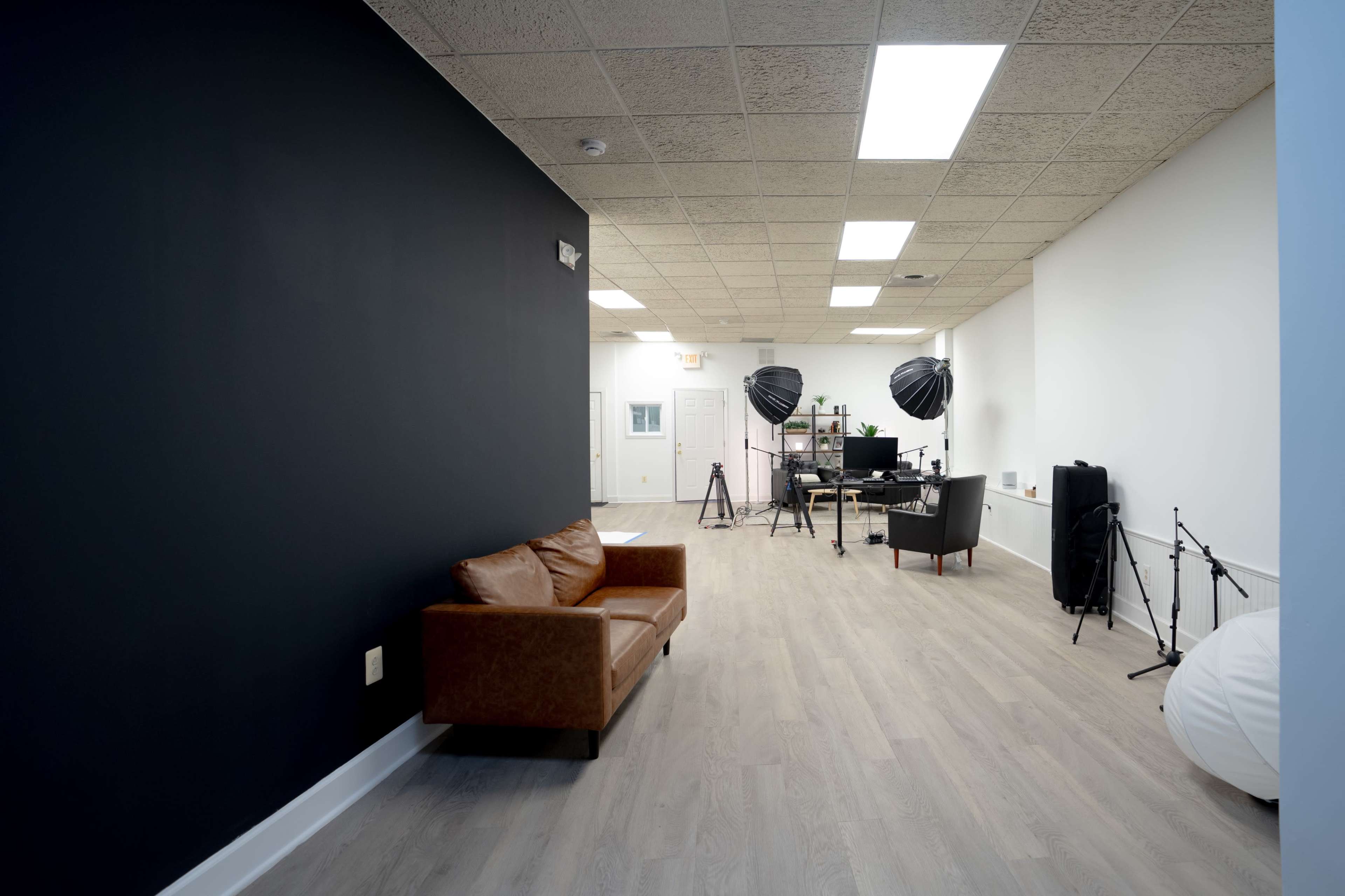 The image shows a spacious, modern room with a dark-colored wall on one side, featuring a leather couch and various photography equipment in the background.