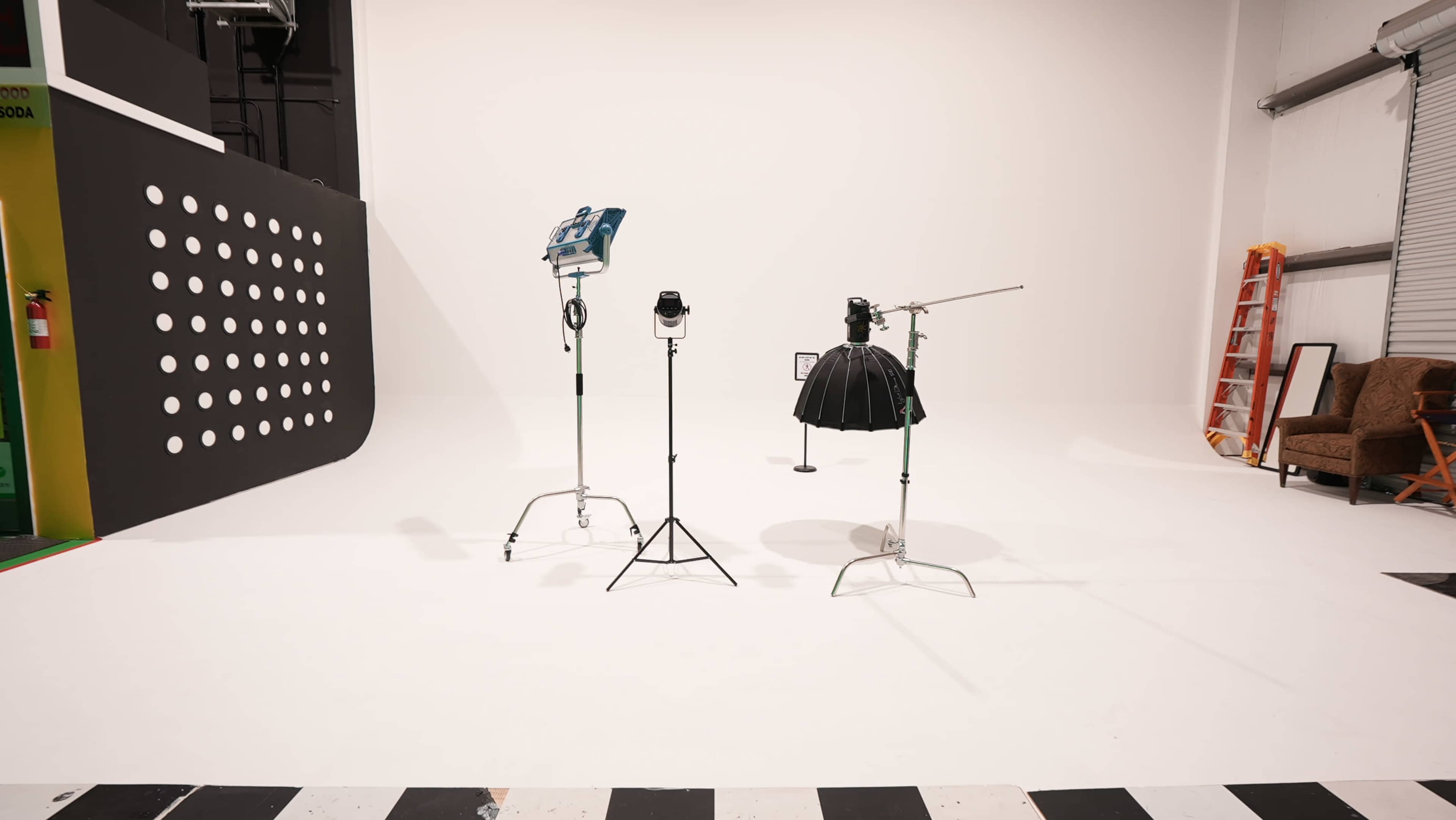 A photography studio is set up with three lighting fixtures and a backdrop, featuring a black skirt-like light modifier on a stand.