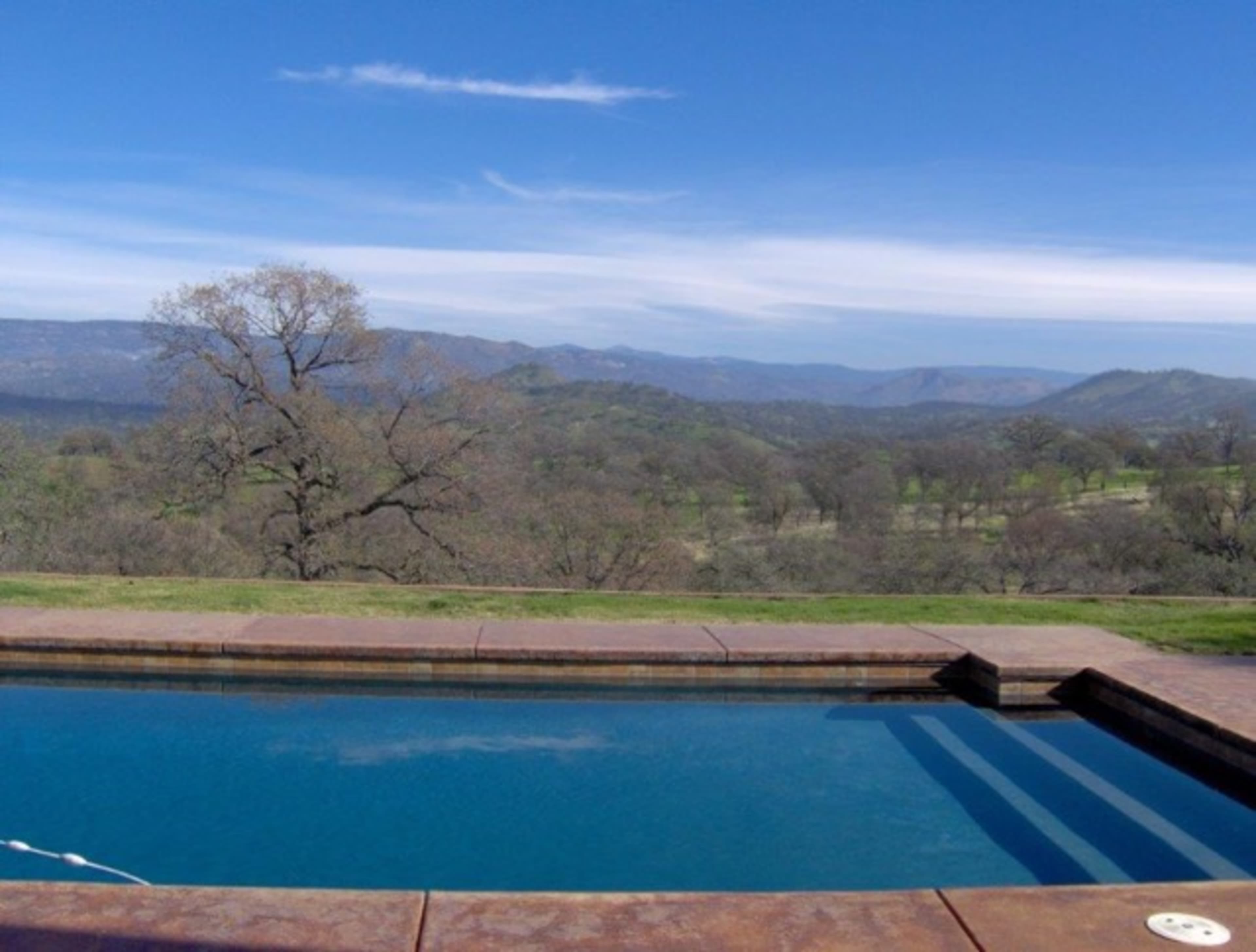 A clear blue swimming pool with a mountainous landscape in the background under a partly cloudy sky.