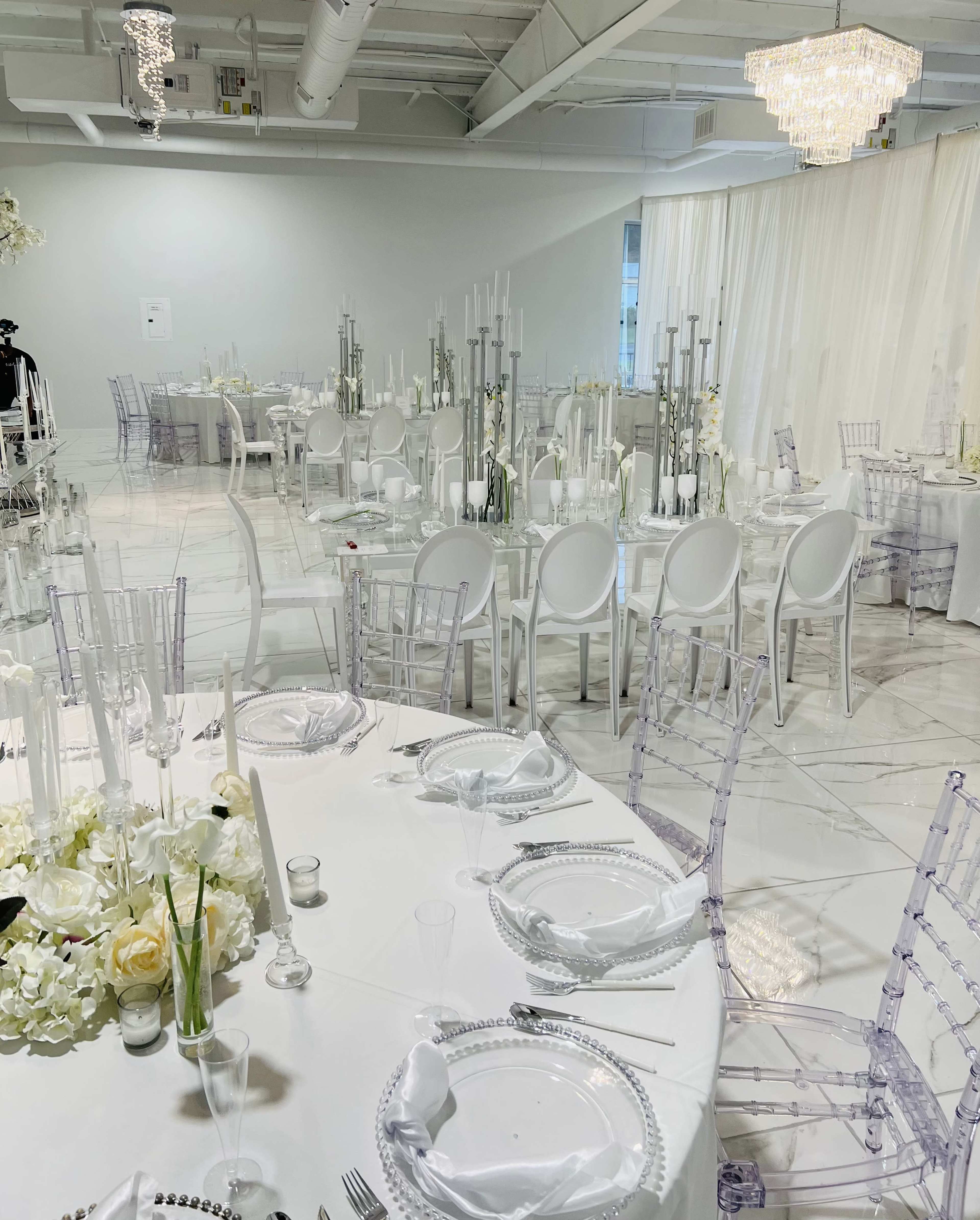 The image shows an elegantly set banquet hall with round tables topped with white tablecloths, crystal candle holders, and floral centerpieces.