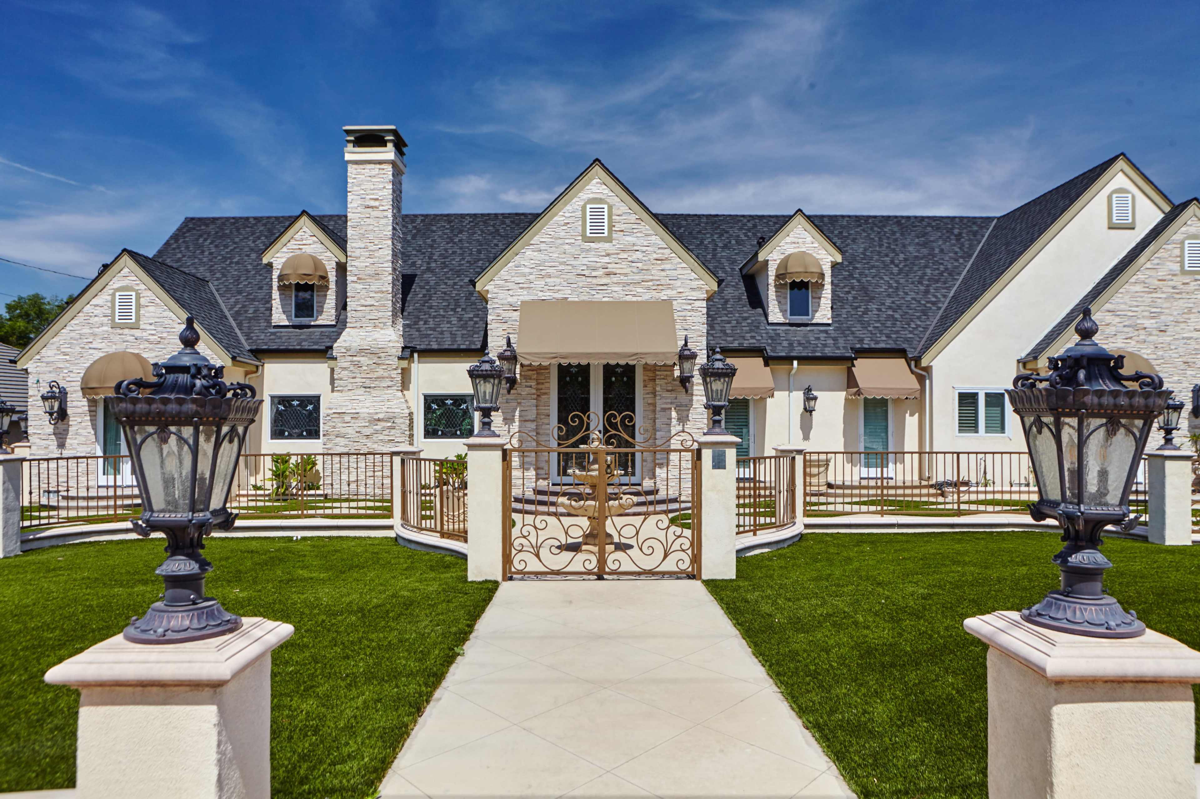 The image shows an elegant, large house with a stone facade, peaked roofs, and decorative lanterns in the foreground.