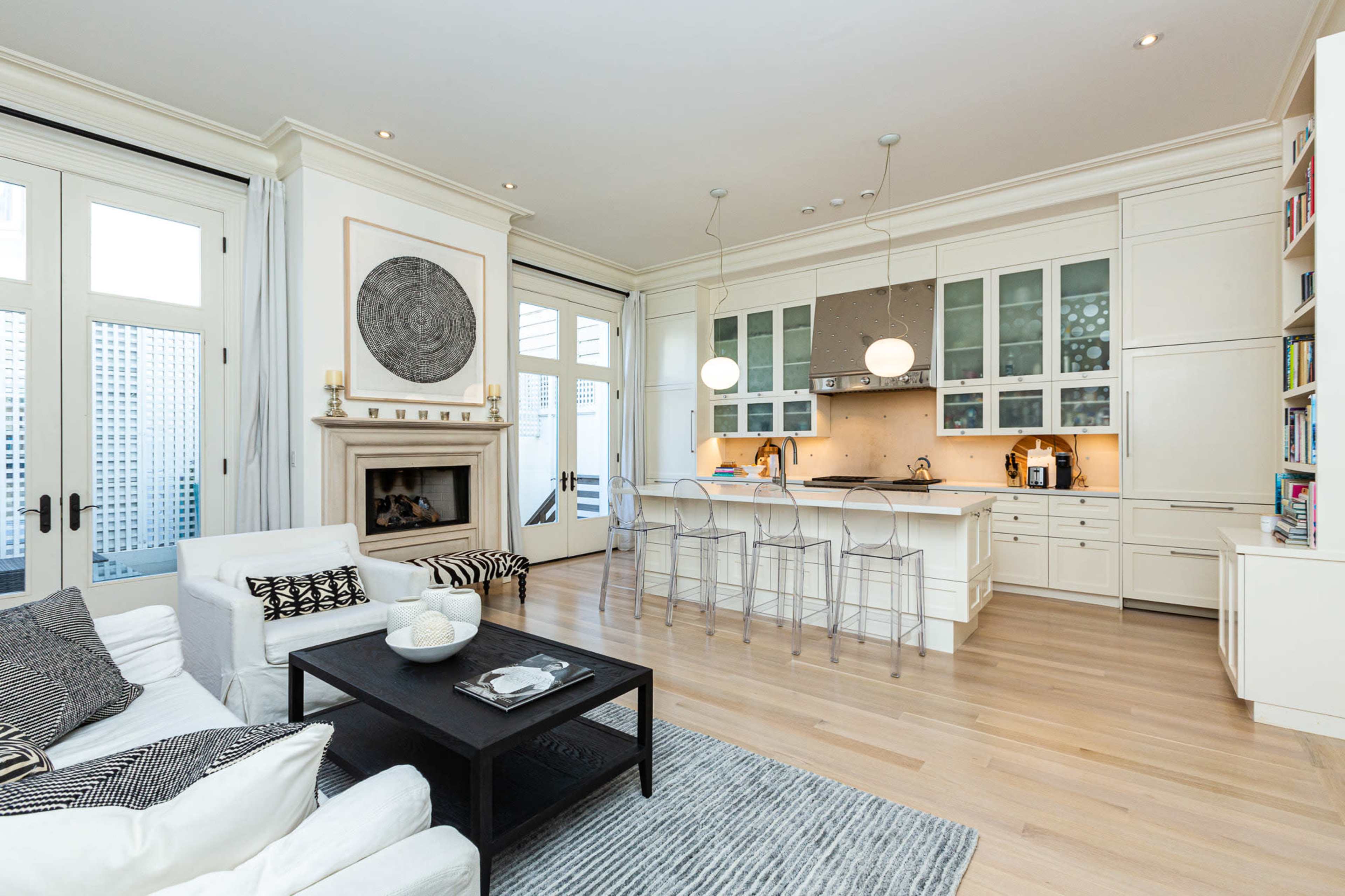 The image shows a modern open-concept living area that features a kitchen with a large island, a fireplace, and a seating area with a white sofa and a black coffee table.