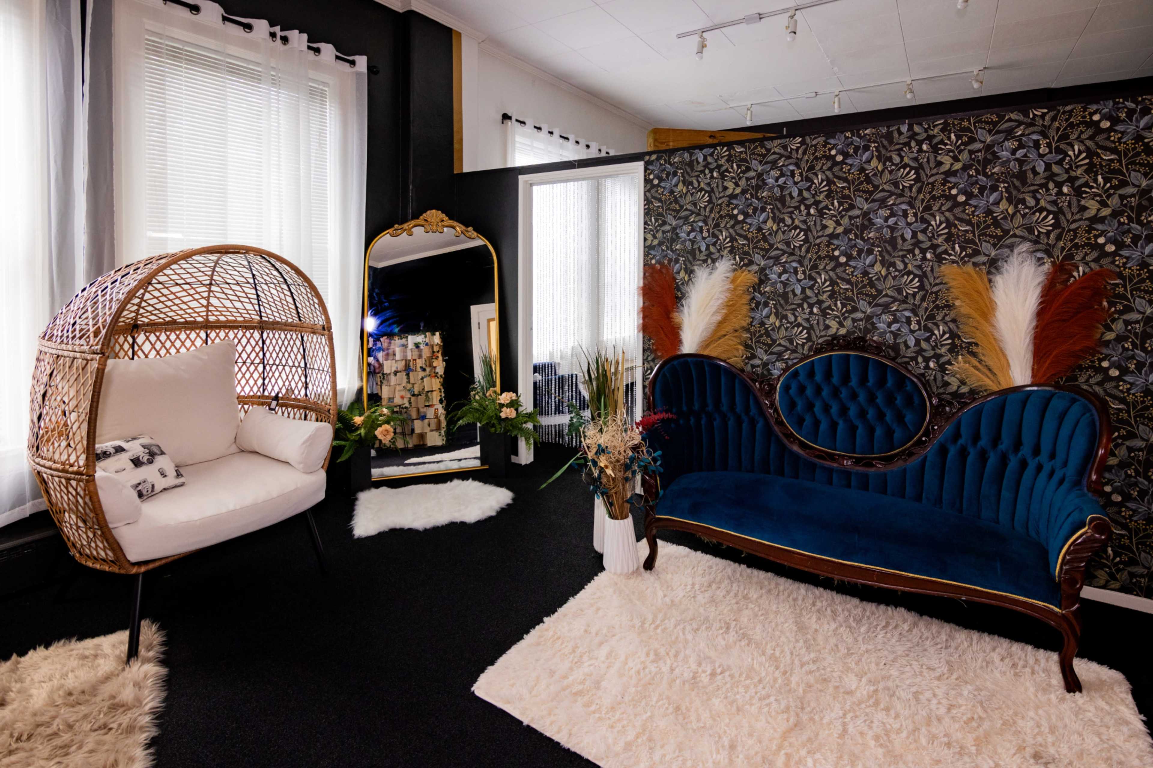 The image features a stylish room with a blue upholstered sofa, a white rattan chair, and a decorative mirror against a floral wallpaper backdrop.