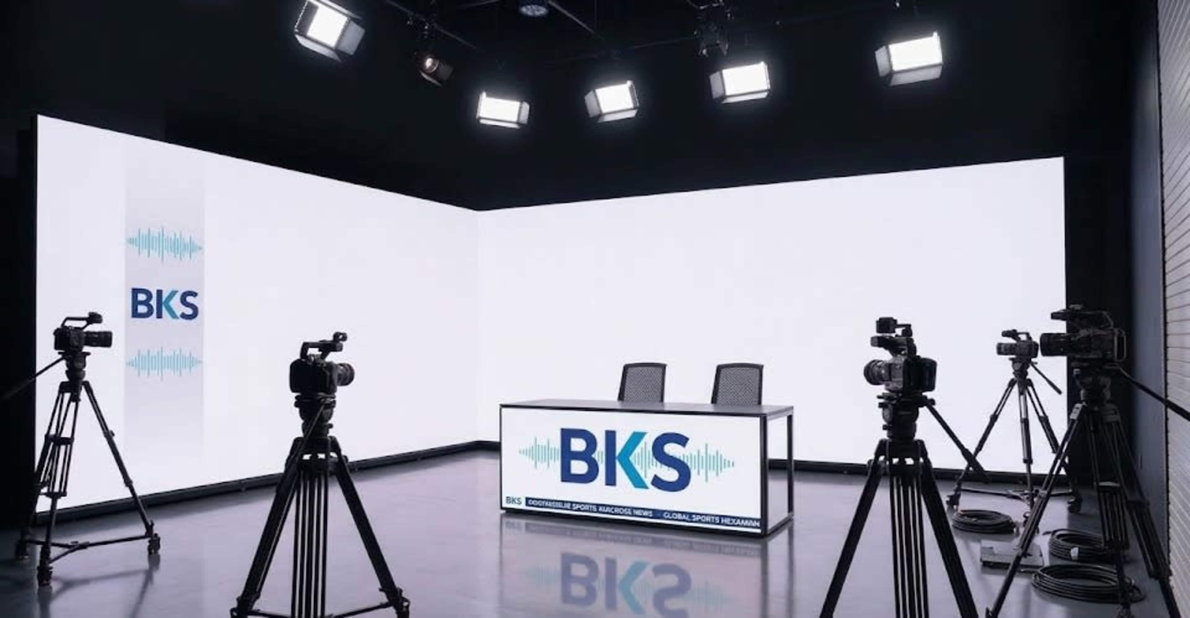 The image shows a modern studio setup featuring a central table with two chairs, surrounded by multiple cameras and large bright lights against a minimalistic backdrop.